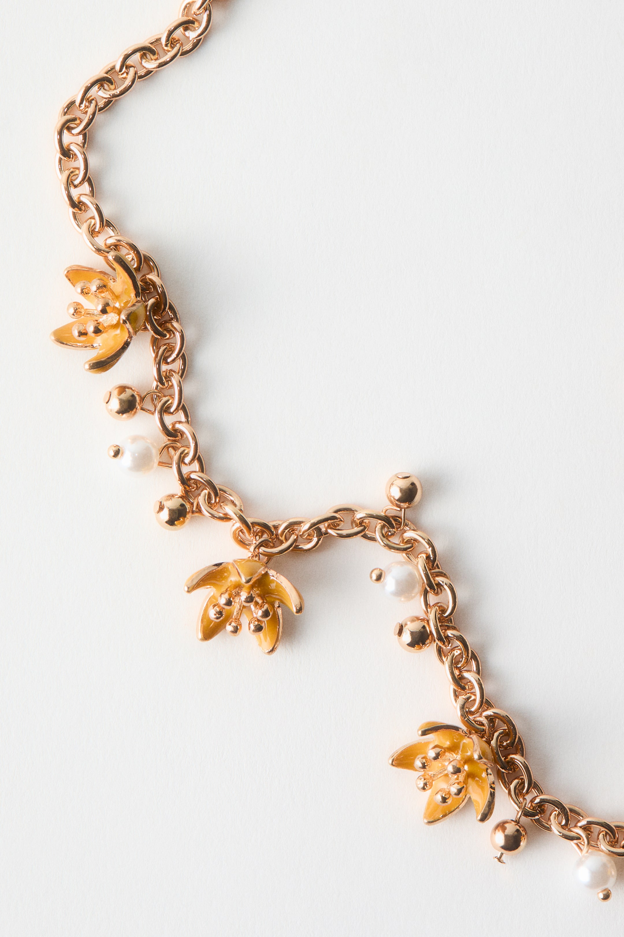 Ver imagen más grande: Un collar de cadena en tono oro rosa presenta dijes de flores esmaltadas en amarillo con pequeñas cuentas en tono dorado en su centro, intercaladas con pequeñas cuentas de perlas blancas y cuentas esféricas en tono dorado. La cadena se curva, mostrando la disposición de sus dijes.