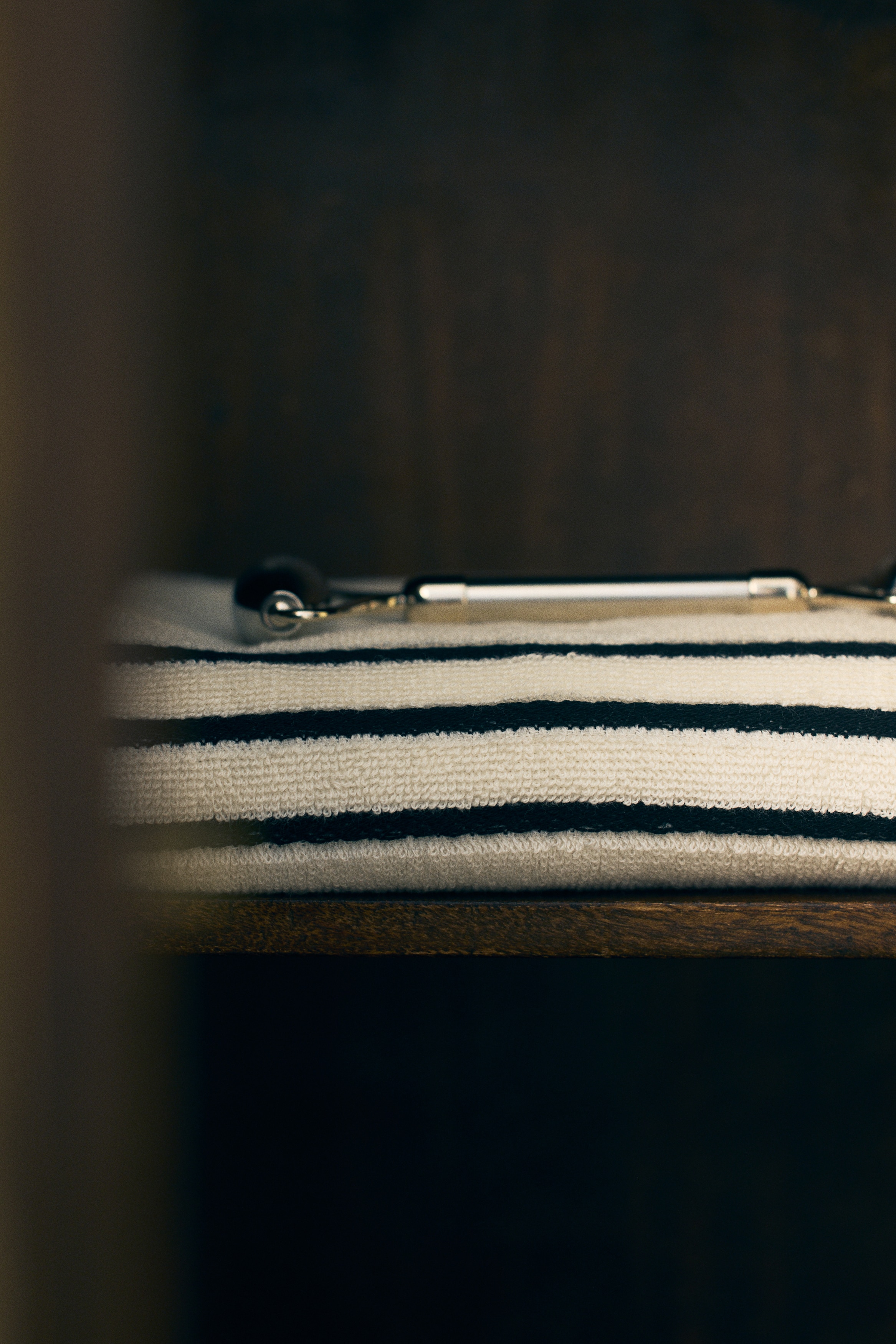 Une serviette de couleur crème est suspendue, pliée sur un crochet noir, affichant trois bandes horizontales noires près de son bord inférieur et un motif de grille noire sur sa partie supérieure.