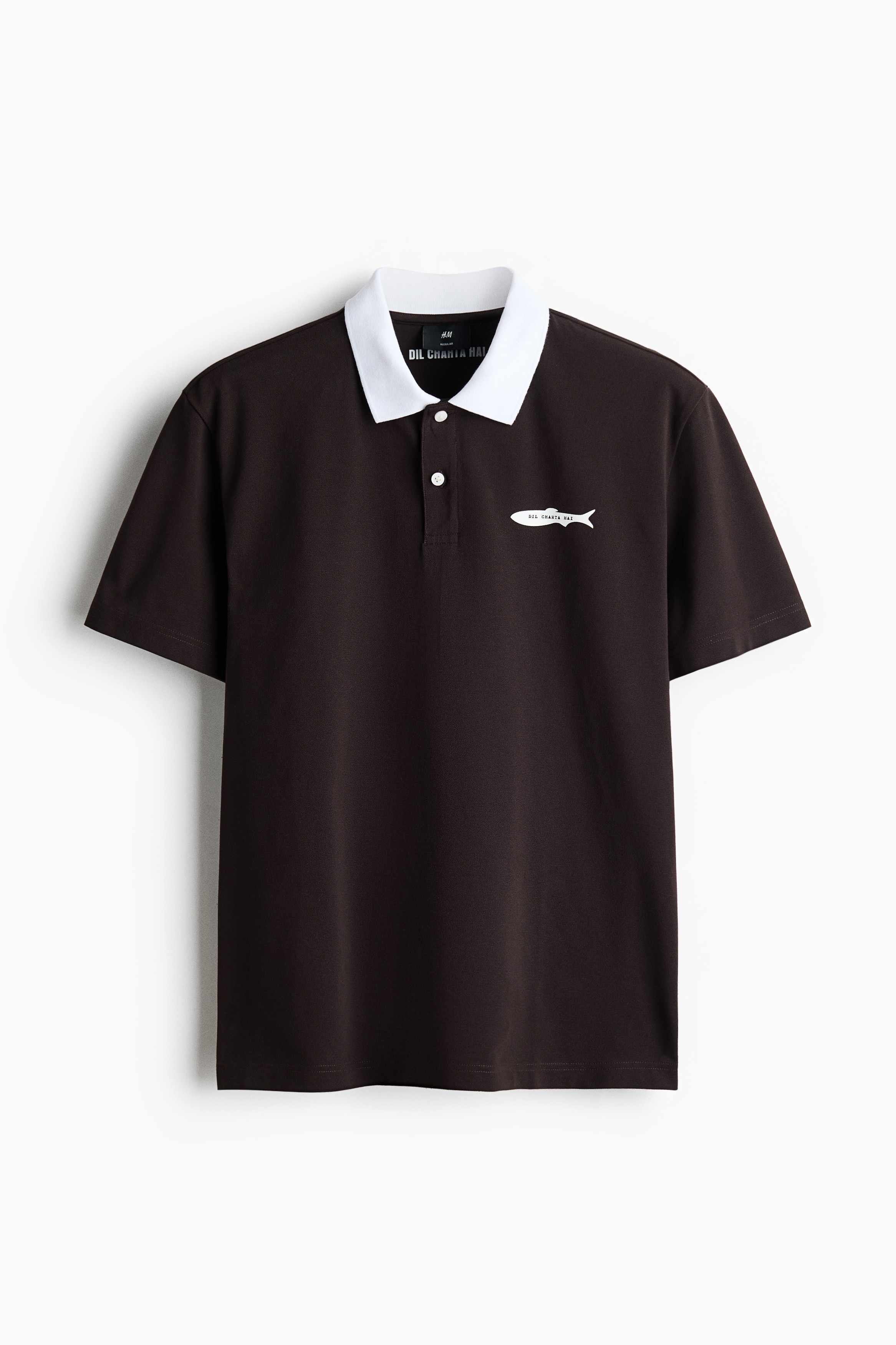 The model is wearing a dark brown polo shirt with a contrasting white collar and a small white fish graphic on the left chest. The short-sleeved shirt features a two-button placket and is styled with beige trousers.