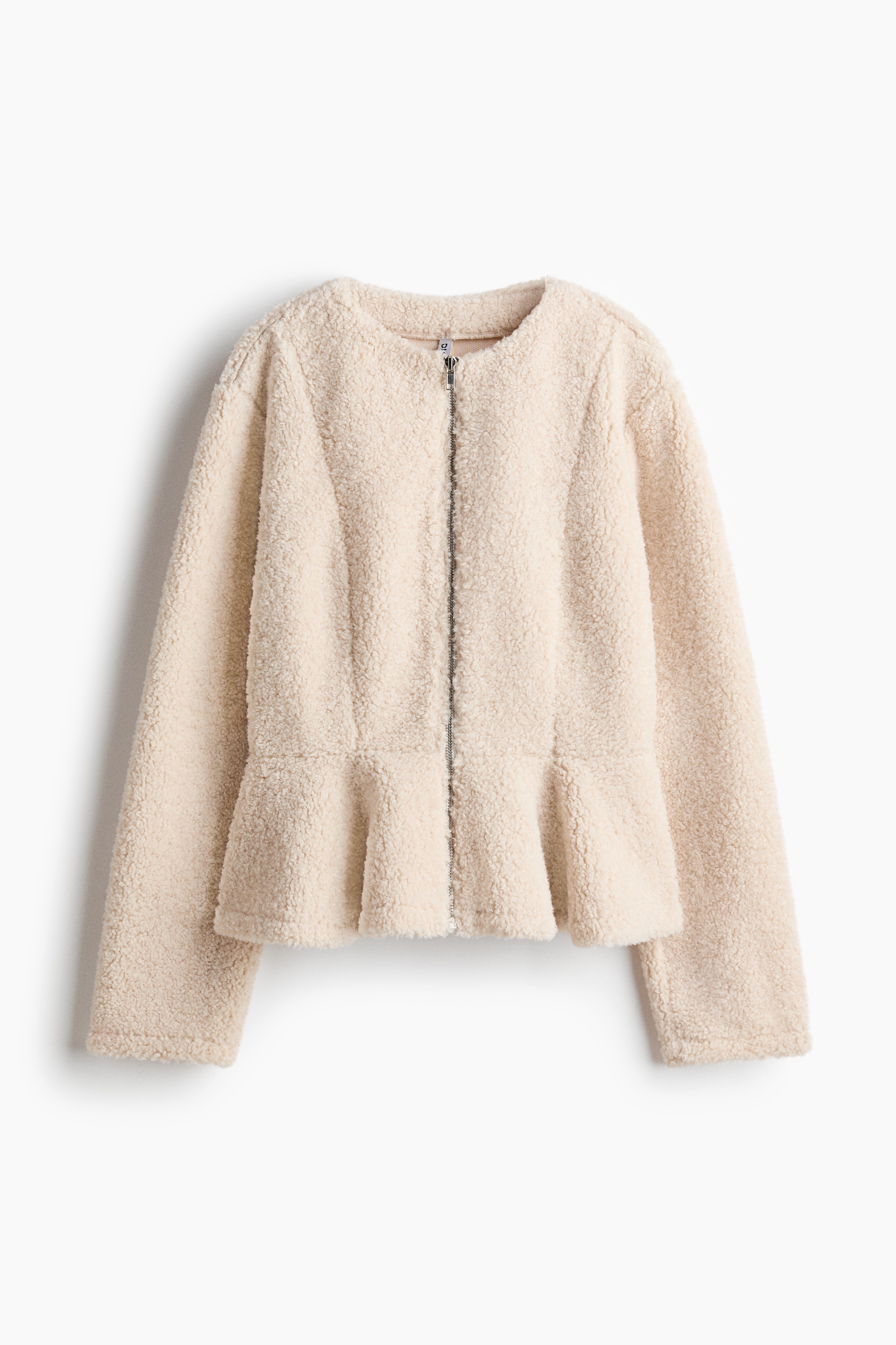 Une veste teddy douce avec un bas peplum évasé est portée par le mannequin, qui regarde par-dessus son épaule. La veste est associée à un jean en denim.