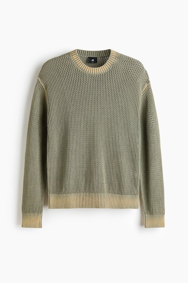 The olive green open-knit sweater is shown from the front, showcasing its textured design. It features a ribbed crew neck, ribbed cuffs, and a ribbed hem, all in a faded beige hue, which also accentuates the raglan shoulder seams. - 1