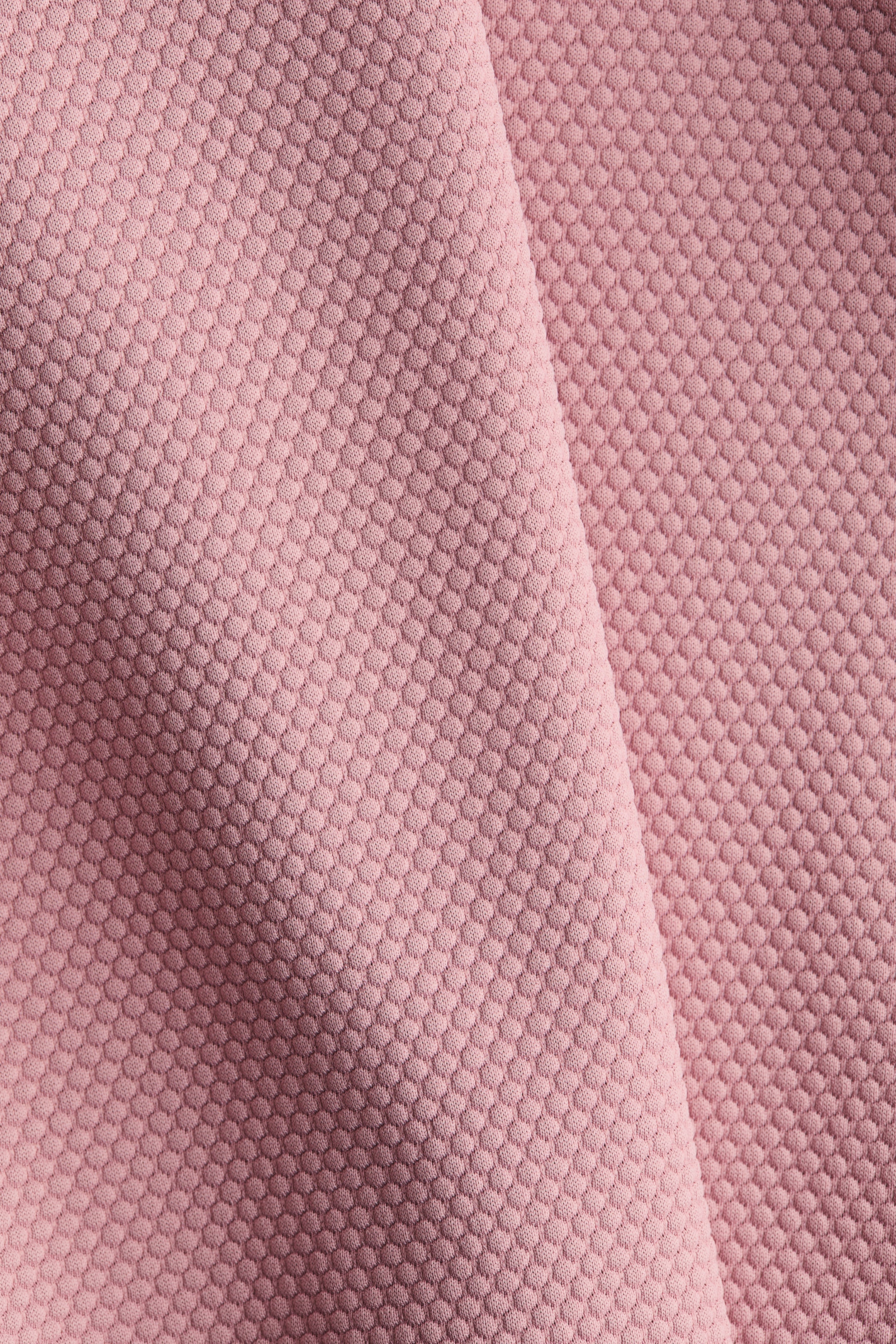View larger image: Pink fabric is displaying a raised, textured honeycomb pattern, and it is draped, forming a diagonal fold.