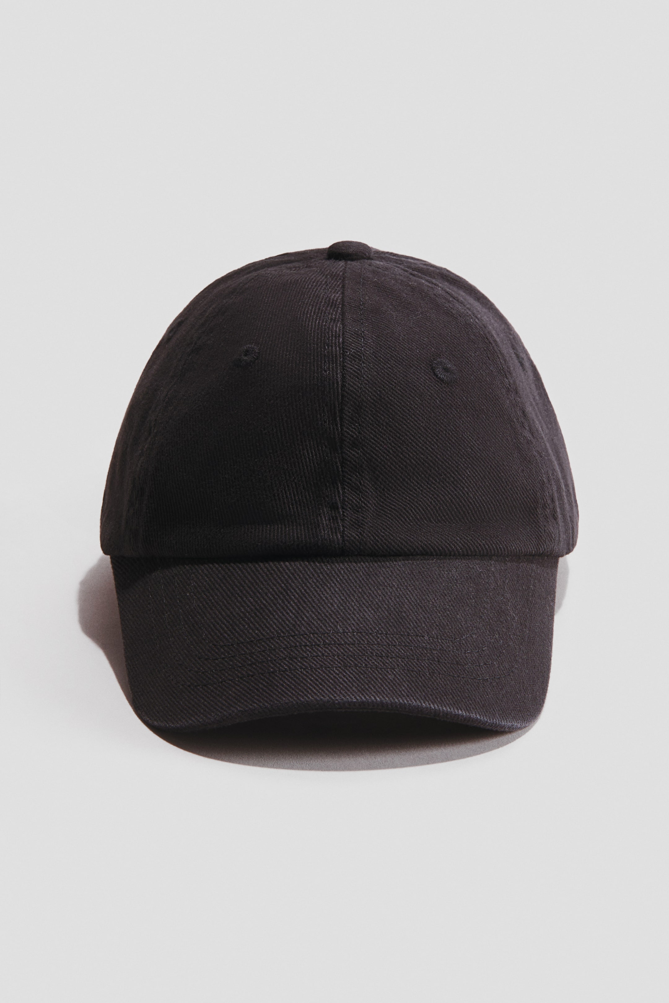 Visa större bild: En svart bomullskeps i twill är vänd framåt, visar en böjd skärm och en toppknapp.