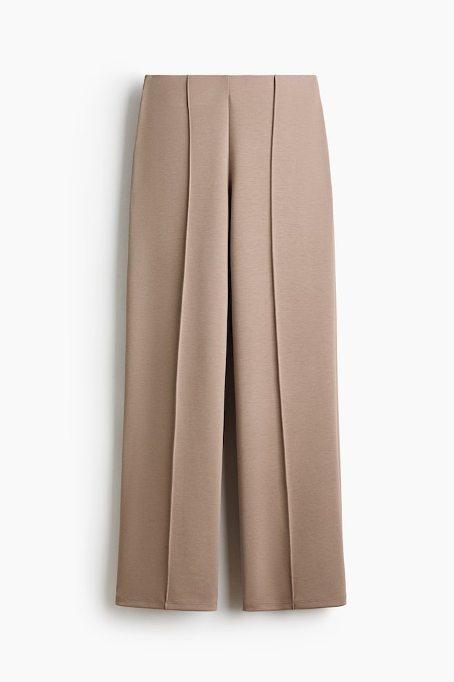 Los pantalones de pierna ancha en color topo presentan una vista frontal, con una pretina plana y pliegues cosidos prominentes que recorren la parte delantera de cada pierna. Terminan con un dobladillo limpio. - 1