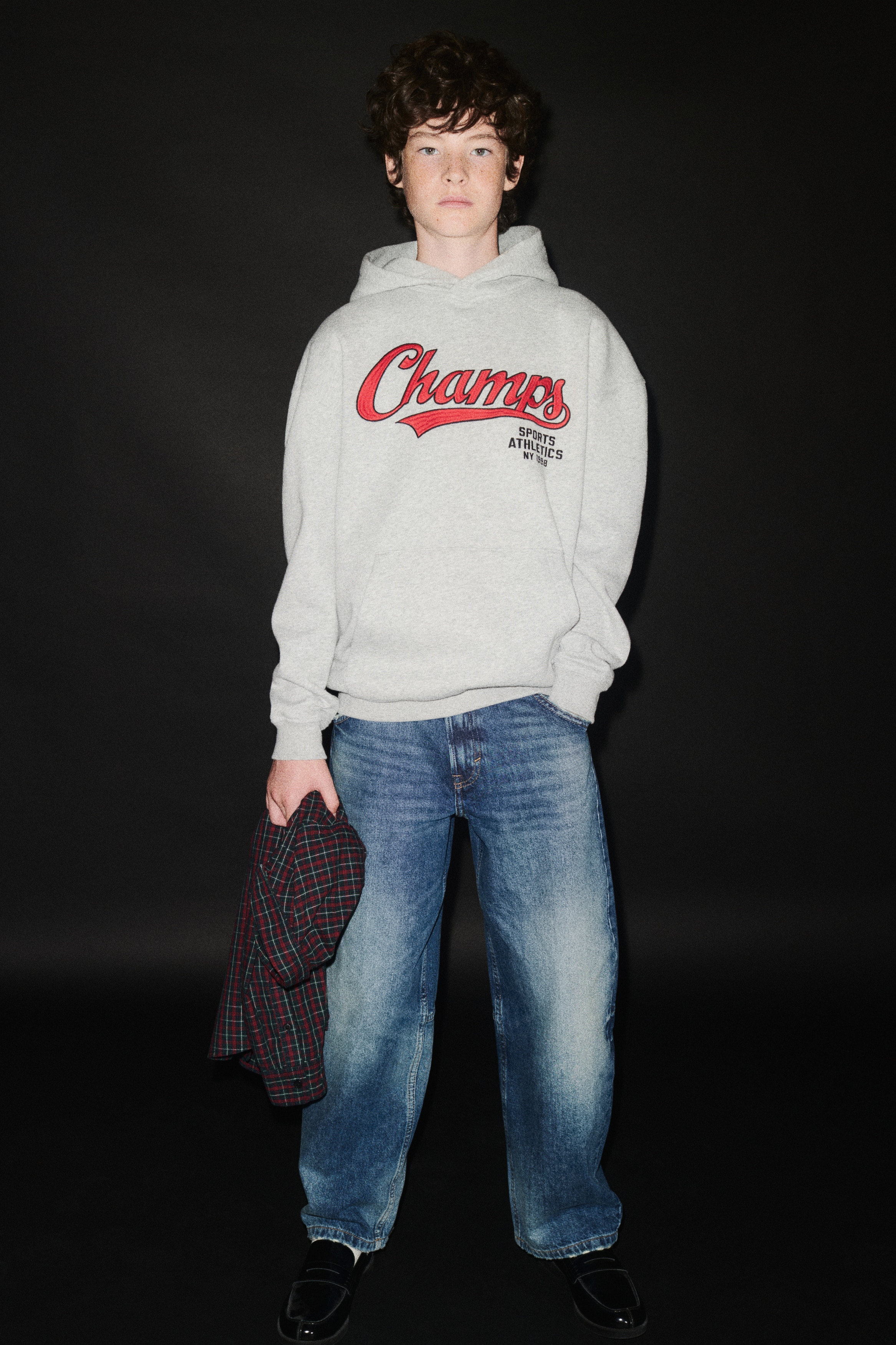 Un paio di jeans in denim blu è ripreso frontalmente, mettendo in risalto una silhouette balloon-leg con lavaggio slavato e vissuto su cosce e ginocchia. I jeans presentano il classico stile a cinque tasche, cuciture a contrasto, chiusura con bottone e zip, e orli leggermente sfrangiati.