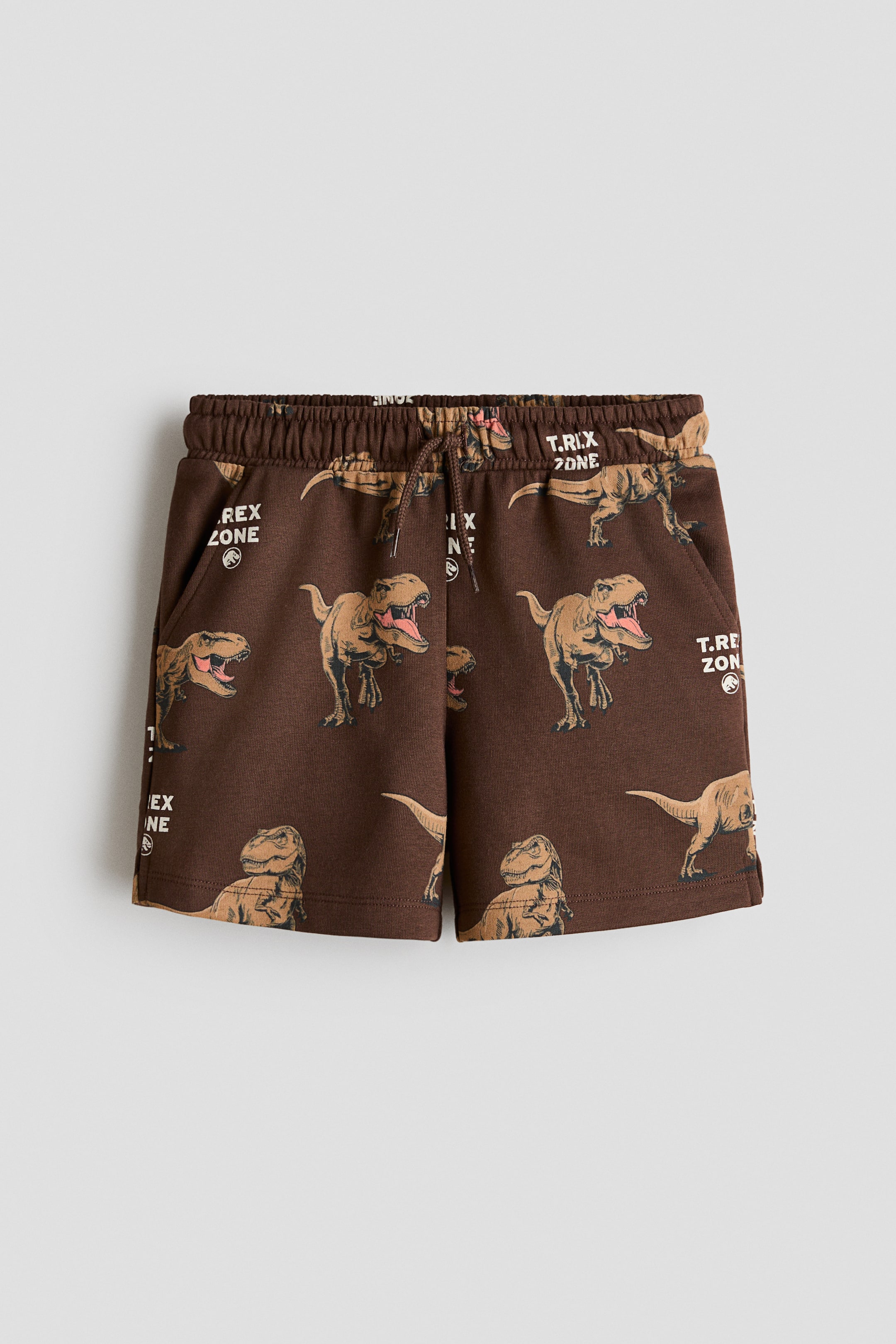Größeres Bild ansehen: Loose-fit braune Sweatshirt-Shorts präsentieren ein Dinosaurier- und "T.REX ZONE"-Printmotiv auf der Vorderseite, mit einem elastischen Bund mit Kordelzug, diagonalen Seitentaschen und kleinen Schlitzen an jeder Seite des Saums.