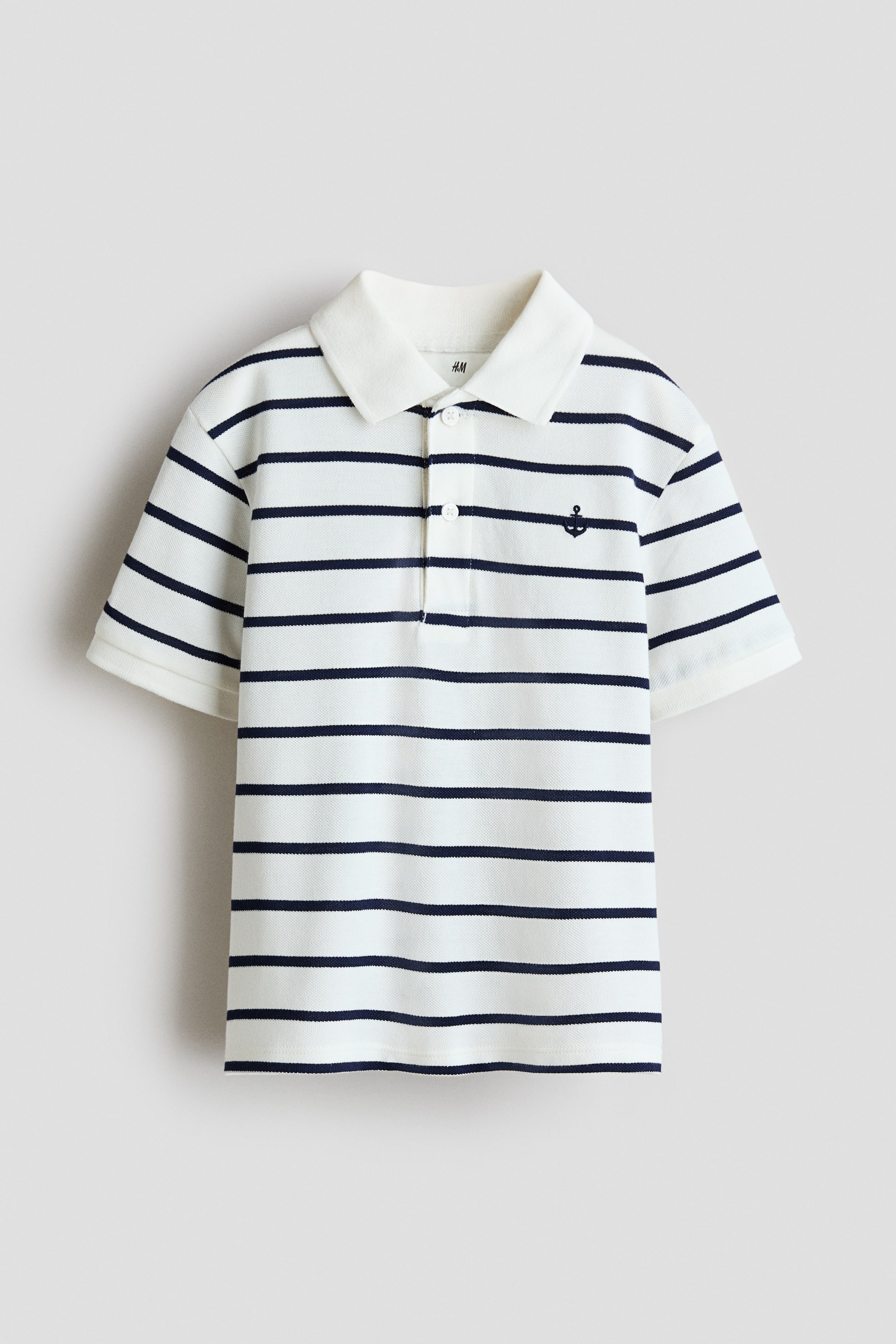 View larger image: A front-facing white polo shirt displays navy-blue horizontal stripes, a white ribbed collar, a two-button placket and short sleeves with ribbed cuffs, with a small navy-blue anchor embroidered on the left chest.