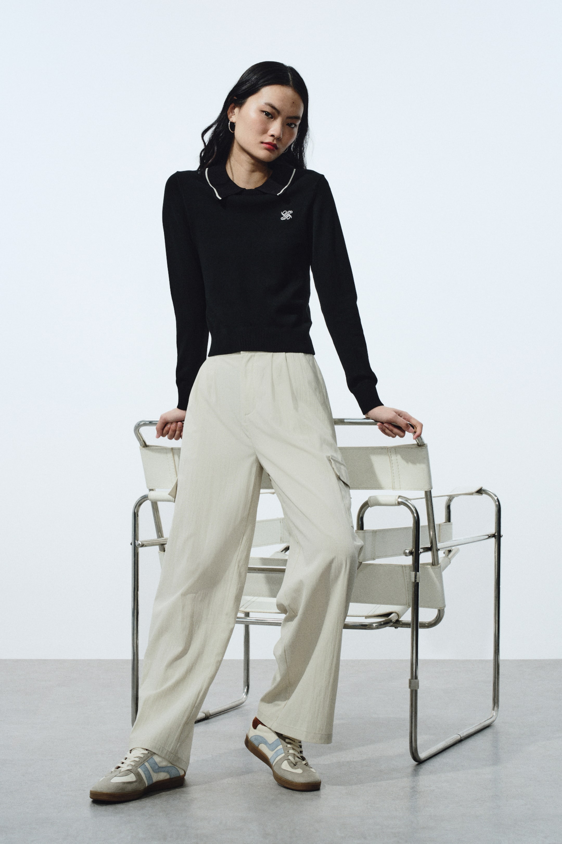 View larger image: A black long-sleeved sweater with a contrasting white Peter Pan collar edged in black layered underneath, a small white embroidered logo on the left chest, and ribbed cuffs and hem.