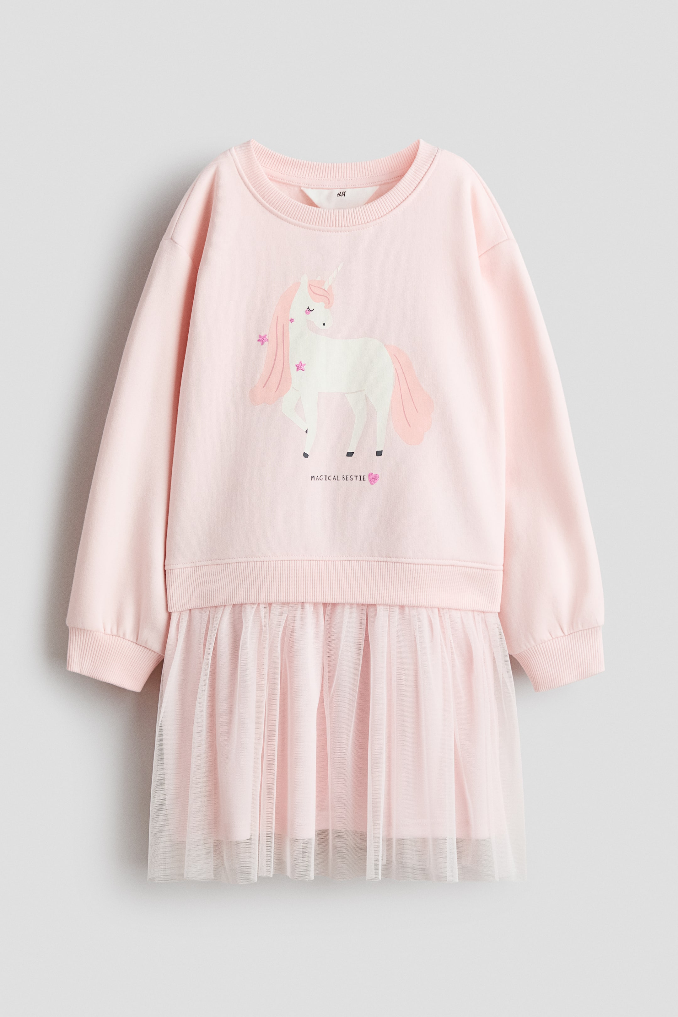 Ingrandisci l'immagine: Un abito in felpa rosa a taglio ampio è presentato FRONTE, caratterizzato da una grafica di unicorno bianco con stelle rosa sul corpetto. Presenta una scollatura rotonda rifinita a coste, spalle scese e maniche lunghe con polsini a coste. La parte inferiore è composta da una gonna di tulle rosa arricciata, sovrapposta a una fodera rosa a tinta unita.