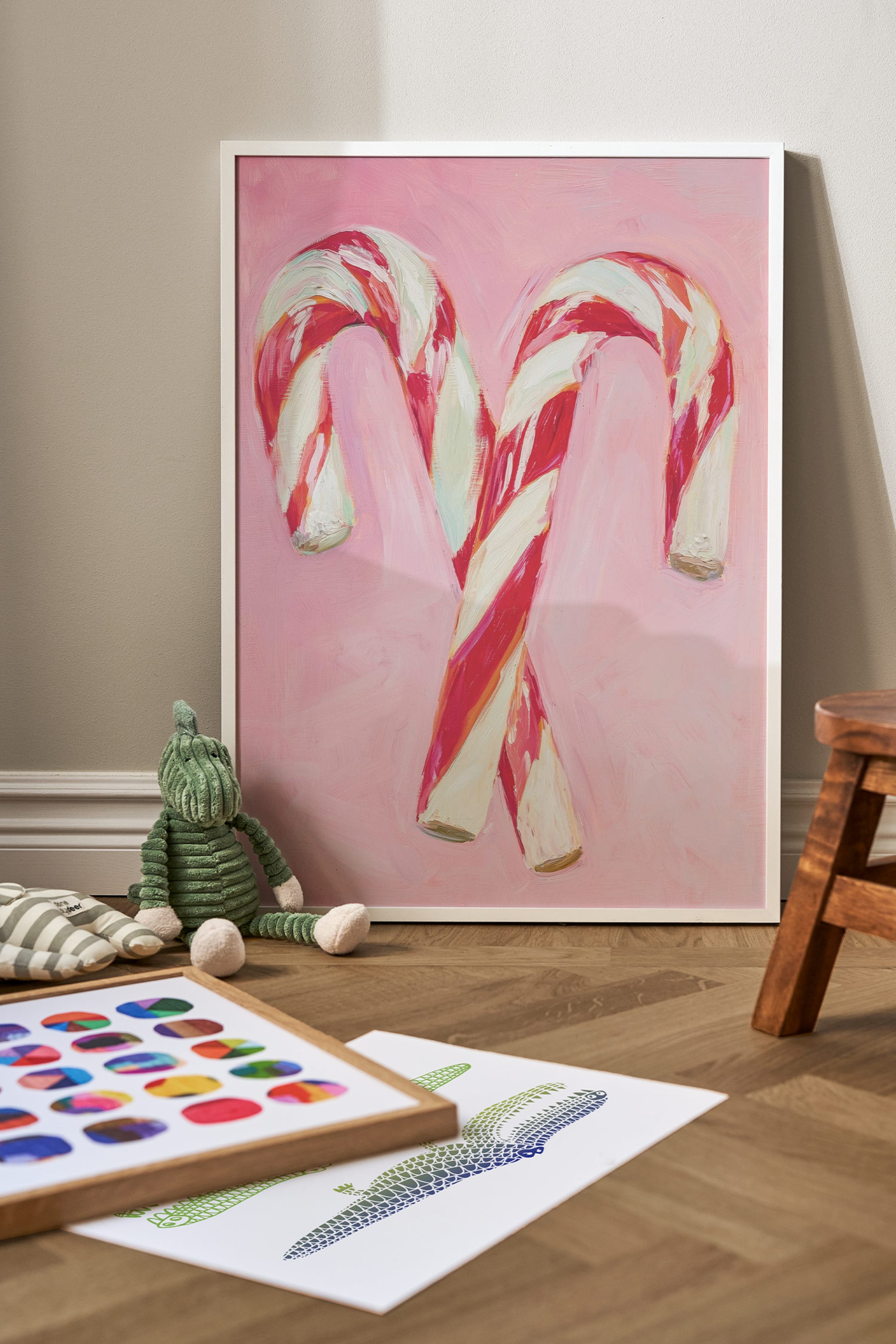 Grotere afbeelding bekijken: Een ingelijste kunstprint toont een schilderij van twee gekruiste zuurstokken met textuurstrepen in rood, roze en wit tegen een effen lichtroze achtergrond. De verticale print is omlijst met een slanke, witte lijst.