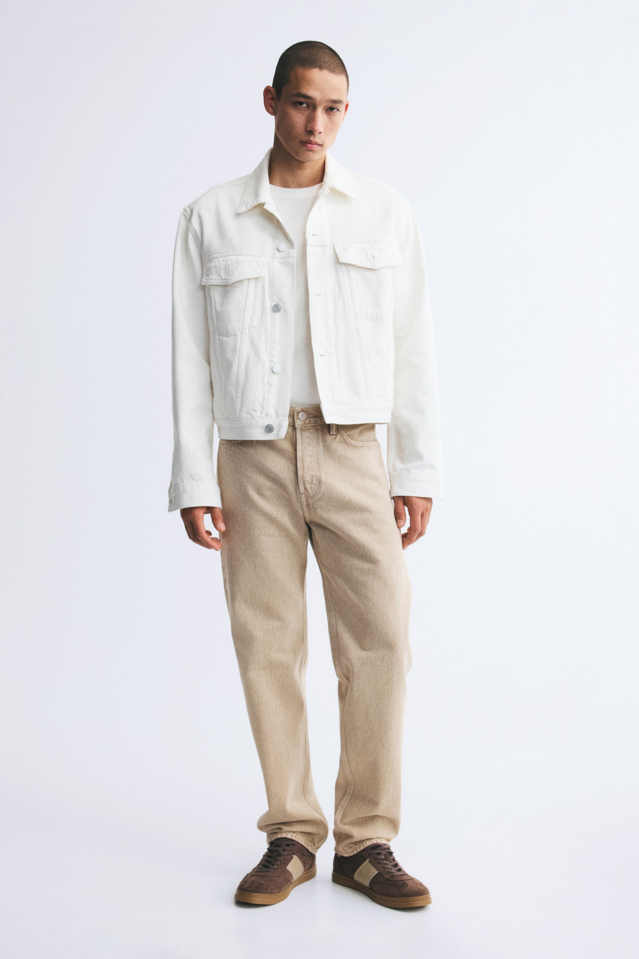 View larger image: Beige five-pocket jeans in sturdy cotton denim, featuring a regular waist and a straight-leg fit, are worn by the model. The jeans are styled with a tucked-in white T-shirt, an open white denim jacket, and brown sneakers.
