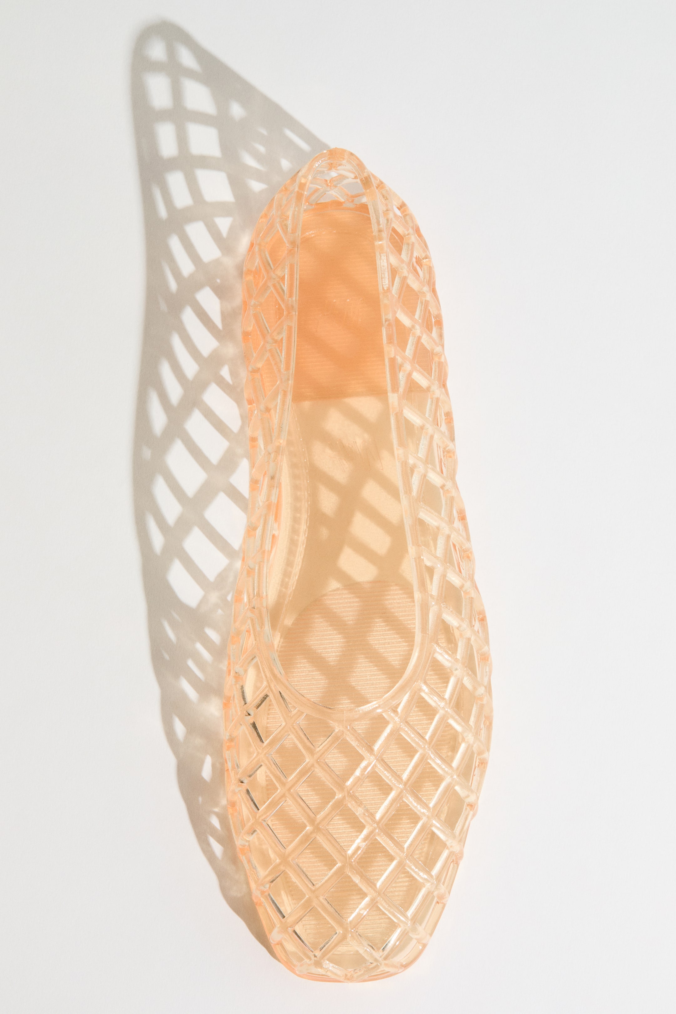View larger image: A single peach-colored translucent jelly flat shoe features an all-over diamond lattice pattern, presented from a top-down view, showcasing its rounded toe and visible inner sole.