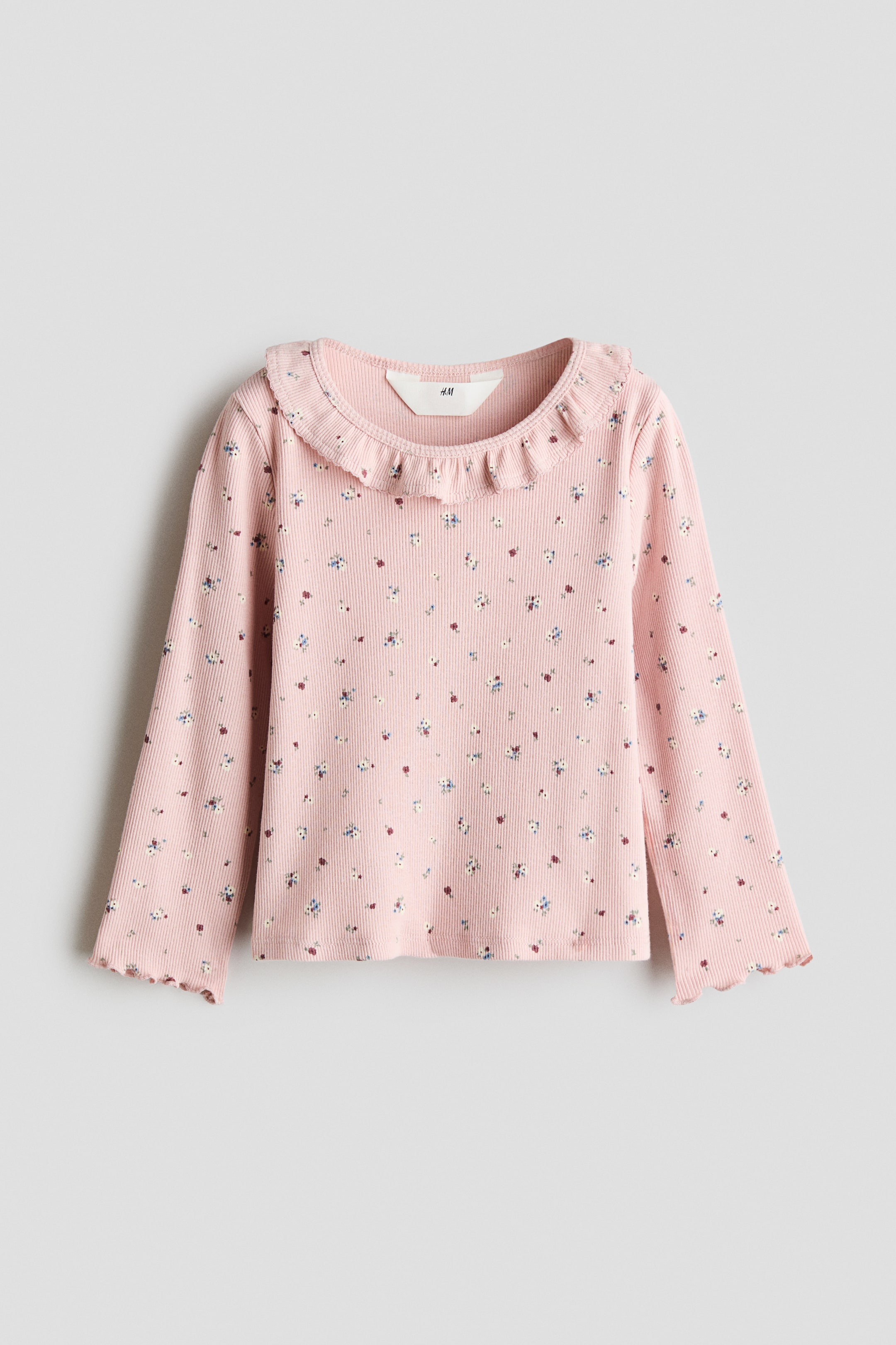 View larger image: A pink, ribbed, long-sleeve top is facing the front, showcasing an all-over print of tiny multicoloured flowers. The top features a ruffled collar around the round neckline and wavy, lettuce-edge cuffs on the sleeves.