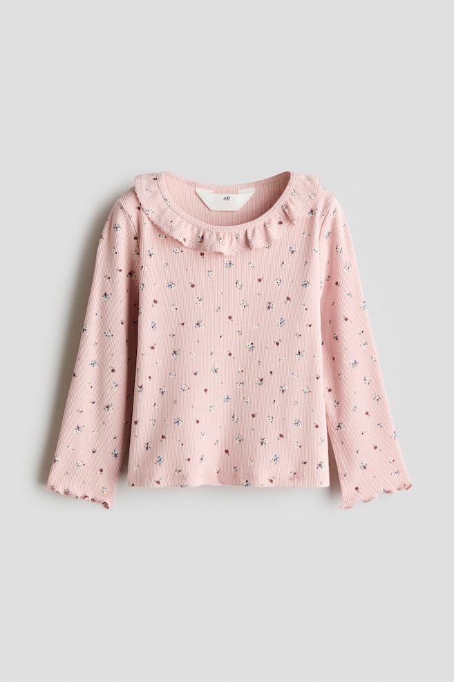 Een roze, geribde top met lange mouwen is van voren te zien en toont een all-over print van kleine, meerkleurige bloemen. De top heeft een gerimpelde kraag rondom de ronde halslijn en golvende lettuce-randboorden aan de mouwen. - 1
