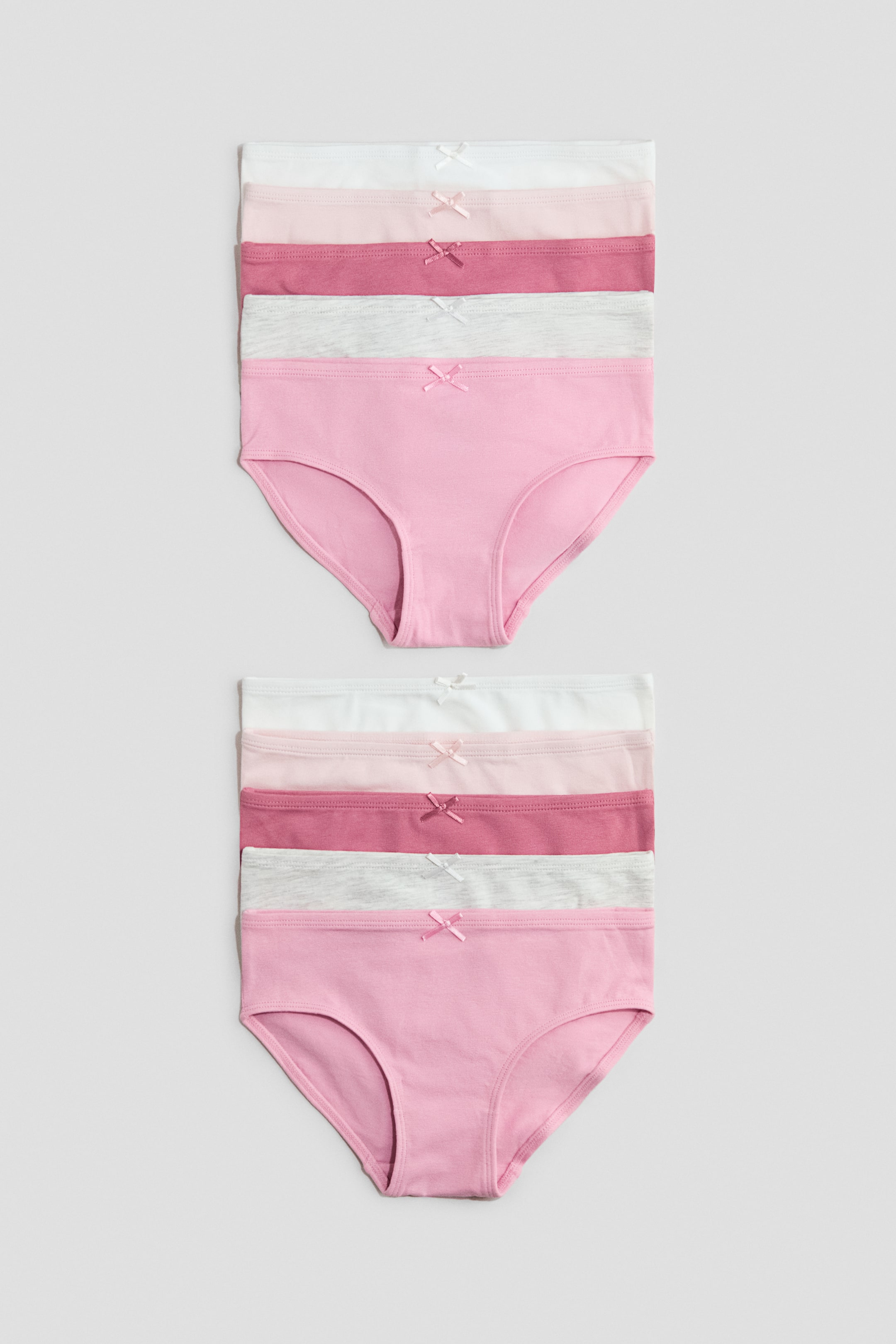 Agrandir l'image: Deux piles de cinq culottes en jersey de coton sont exposées, chacune ornée d'un nœud en satin décoratif centré sur la ceinture avant. Les culottes se déclinent en plusieurs couleurs, notamment blanc, rose clair, rose foncé, gris clair chiné et rose, avec la culotte du bas de chaque pile entièrement visible de face.