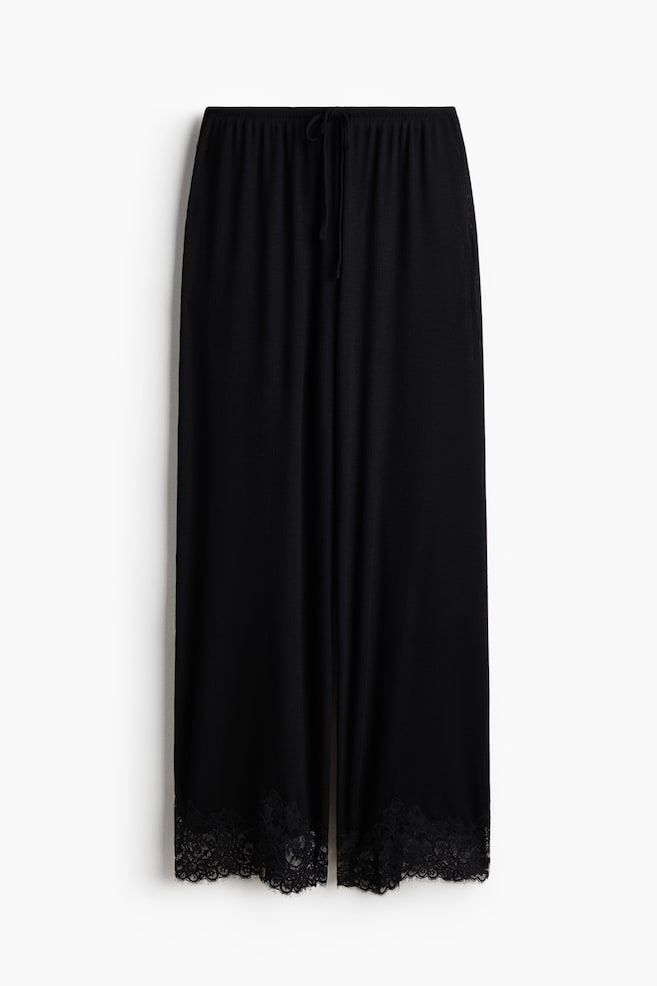 Pantaloni neri a gamba larga presentati frontalmente, caratterizzati da una texture a coste e una fascia elastica in vita con un laccio a vista. Gli orli delle gambe mostrano un bordo in pizzo nero. - 1