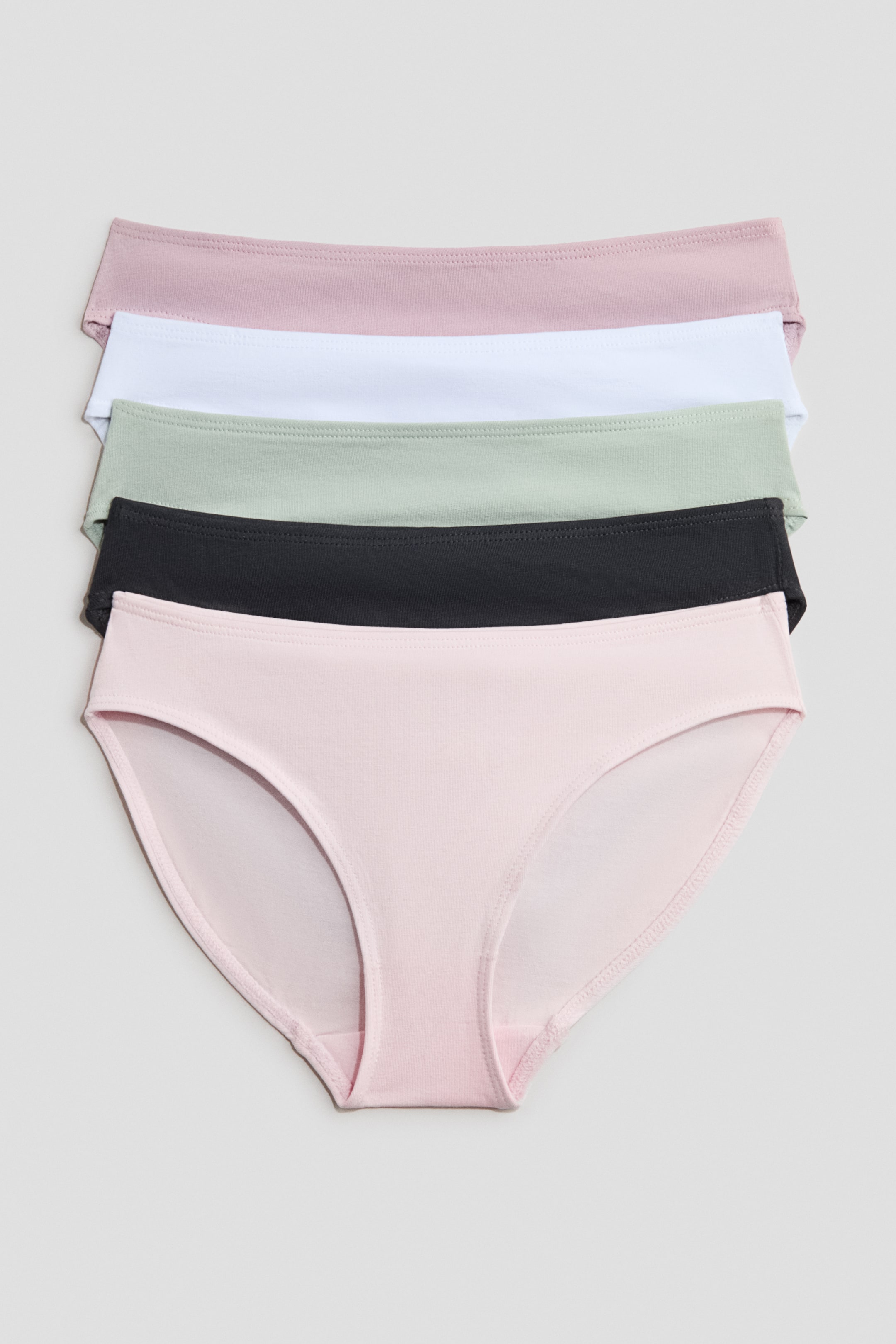 View larger image: "Soft cotton jersey briefs with a lined gusset are showcased from the front, stacked with the bottom pair in light pink, followed by black, light green, white, and a dusty pink pair at the top."