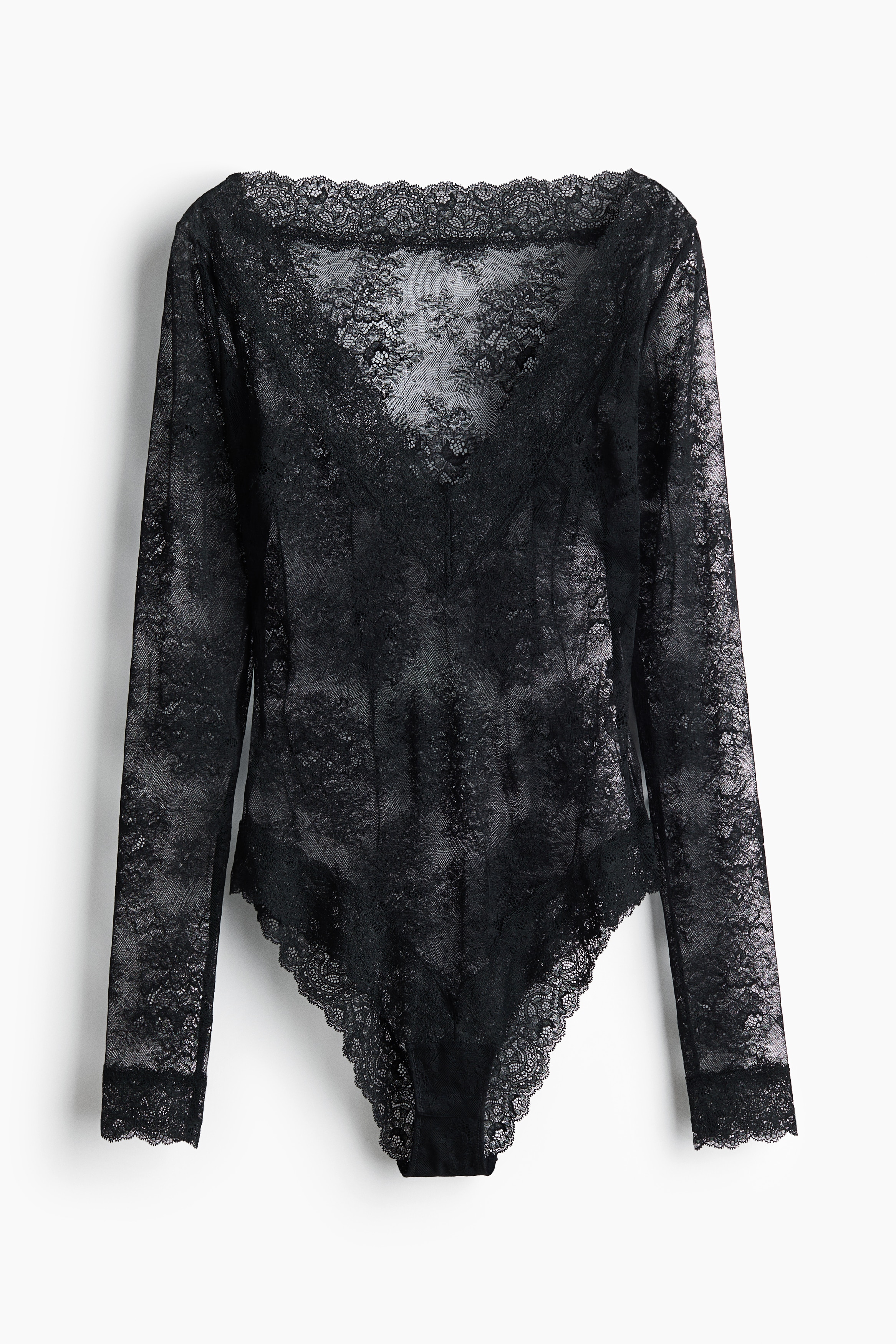 En svart bodysuit med lång ärm i transparent blommig spets bärs av modellen, som sitter med benen i kors. Bodysuiten har en djup V-ringning med dekorativ vågig spetskant.