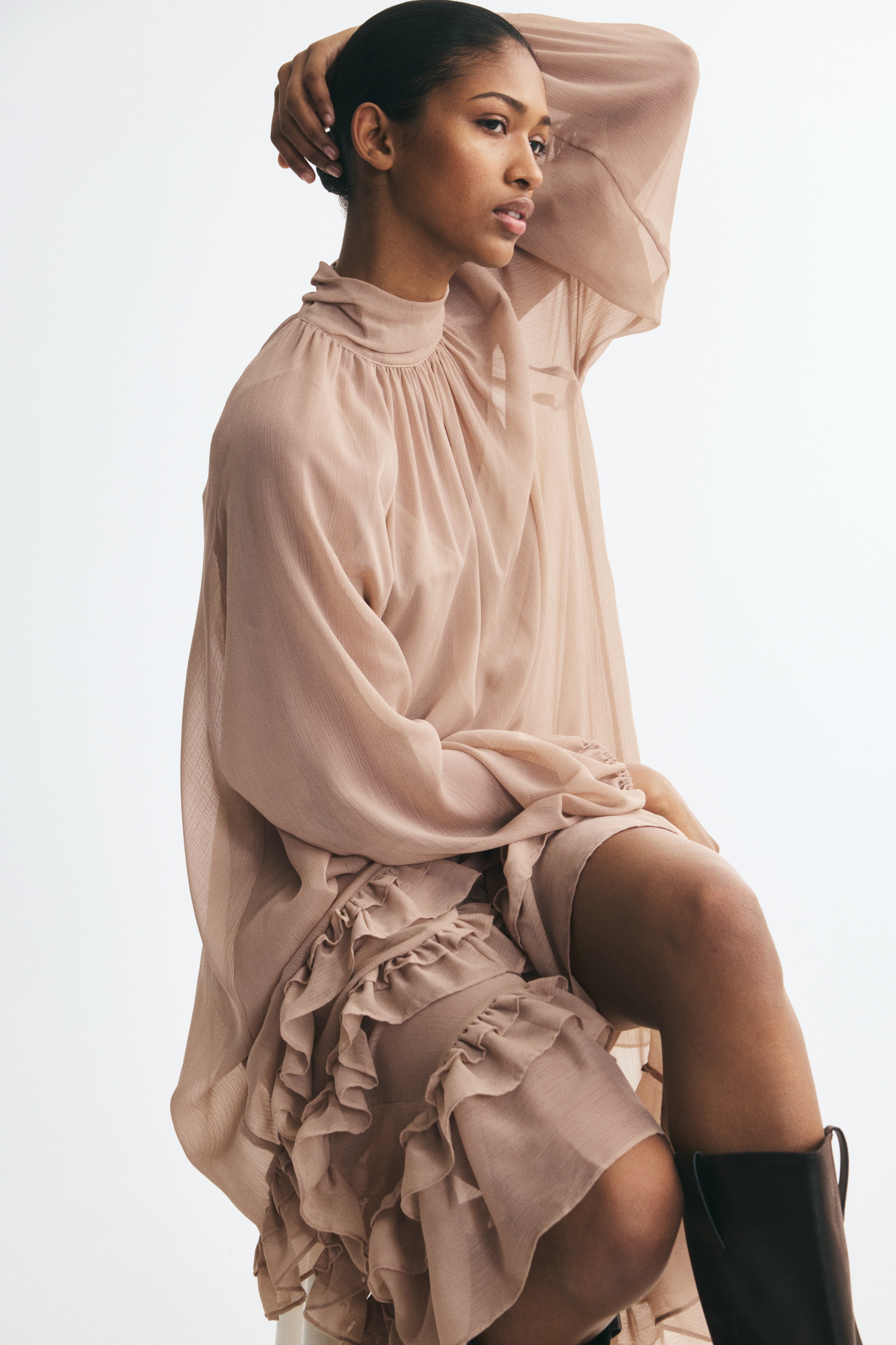 This dusty pink chiffon dress is shown from the front, featuring a high gathered mock neck and long balloon sleeves with elasticated cuffs. The loose, relaxed-fit silhouette flows into a tiered skirt decorated with three rows of ruffled panels near the hem.