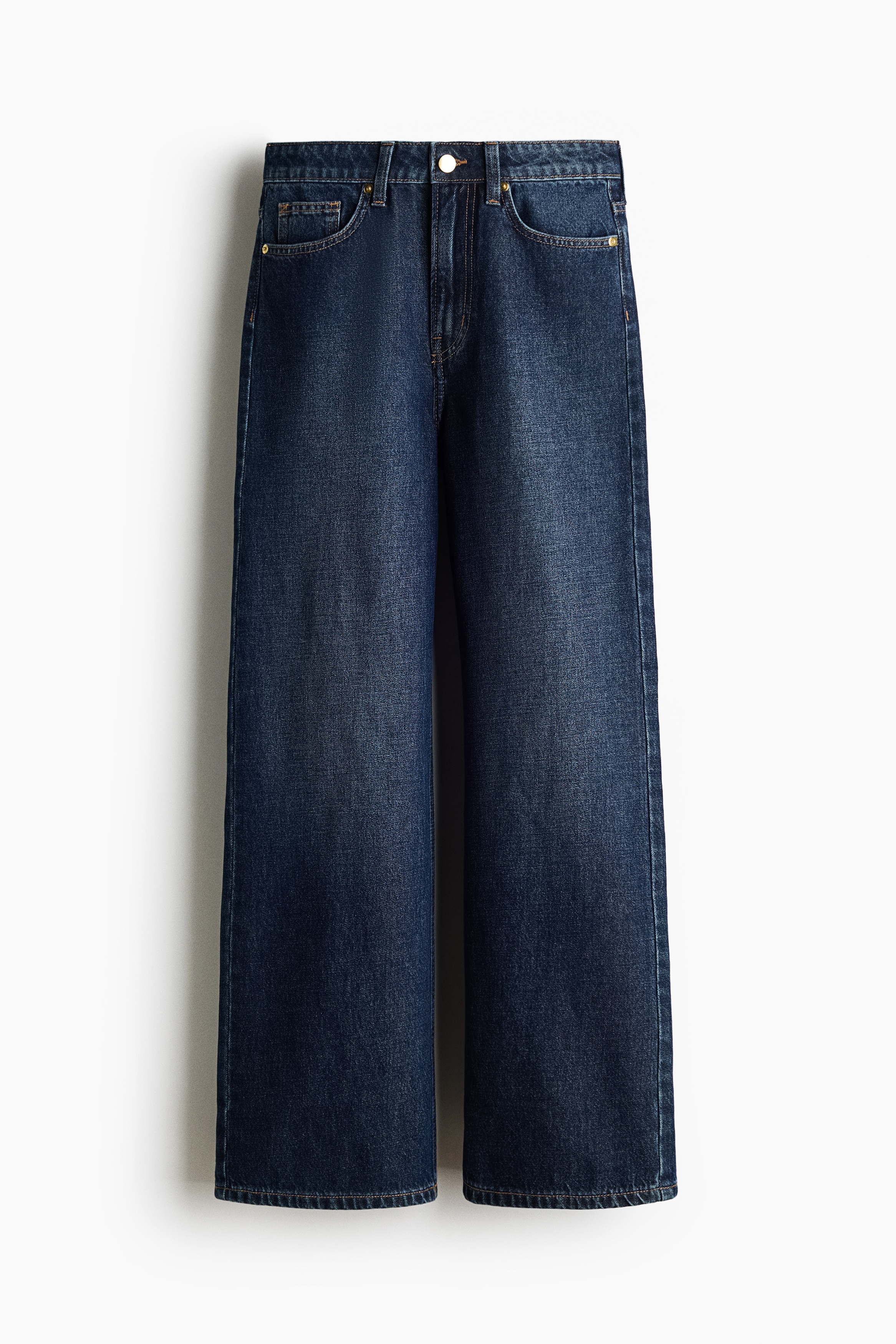 High-waisted, dark blue denim jeans in a straight-leg cut are being worn by the model. The jeans are styled with a tucked-in, matching denim blouse, a black belt featuring a large gold-tone buckle, and white flat shoes.