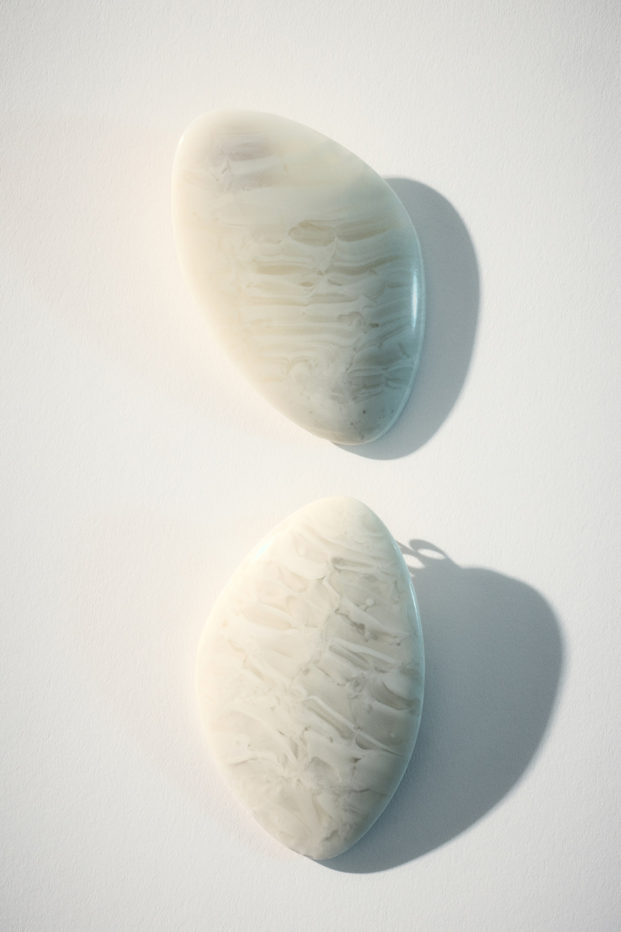 View larger image: Two smooth, irregularly shaped forms lie flat, each showcasing a polished, translucent surface with subtle swirling patterns in white and light gray. They cast soft shadows.