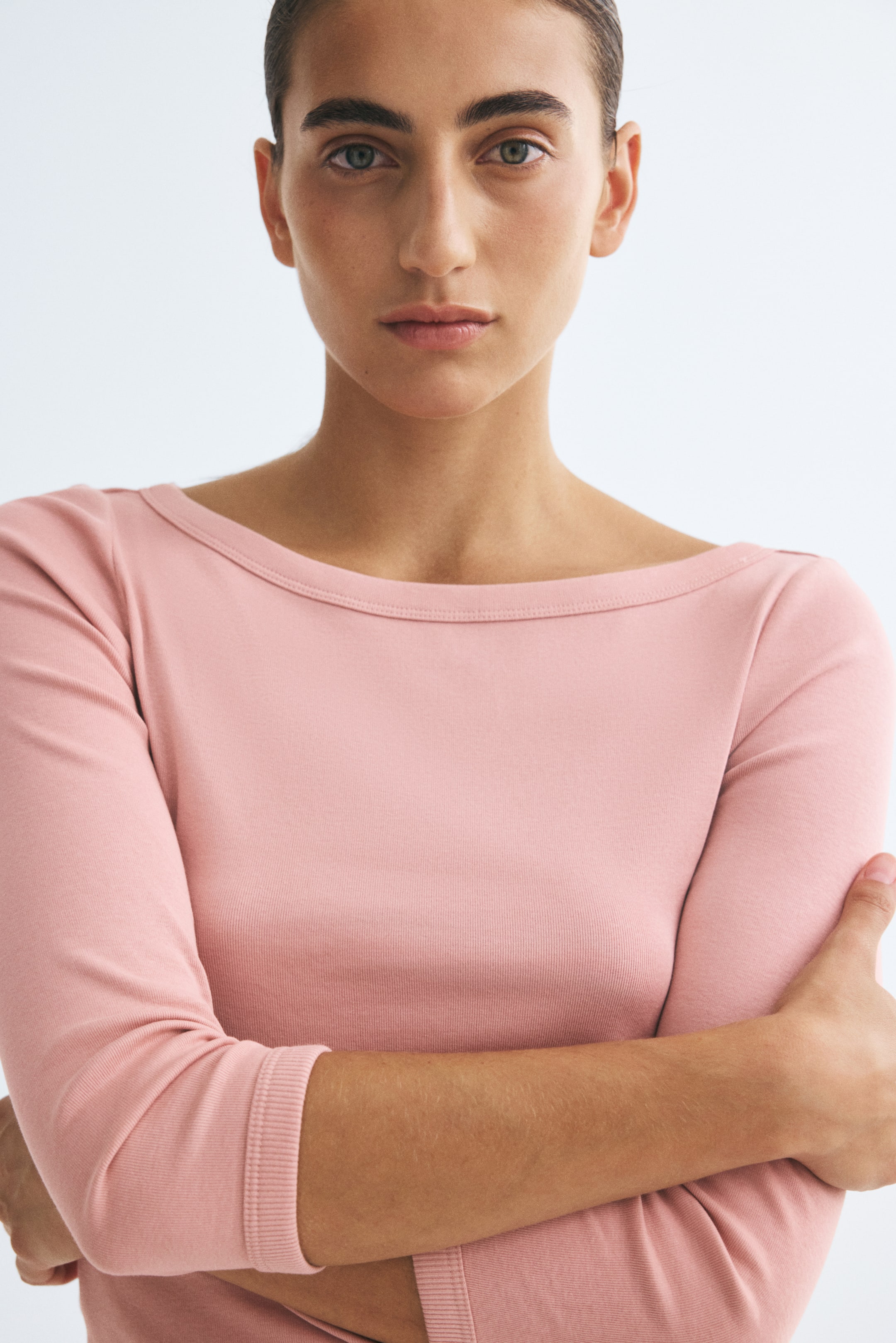 Visa större bild: En rosa figursydd topp i smal ribbad jersey bärs av modellen, som poserar med korsade armar. Toppen har en vid båtringning och långa ärmar.