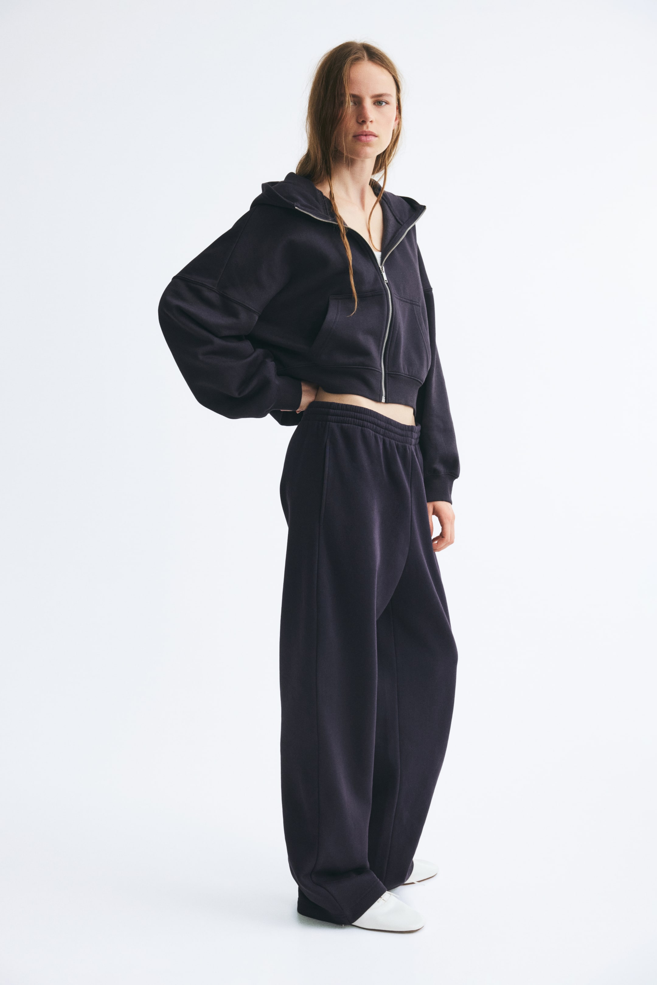 View larger image: Track pants in dark purple cotton-blend sweatshirt fabric are worn by the model, featuring a high-rise, elasticized smocked waistband and a relaxed, straight-leg fit. The pants are styled with a matching cropped zip-up hoodie and white shoes.