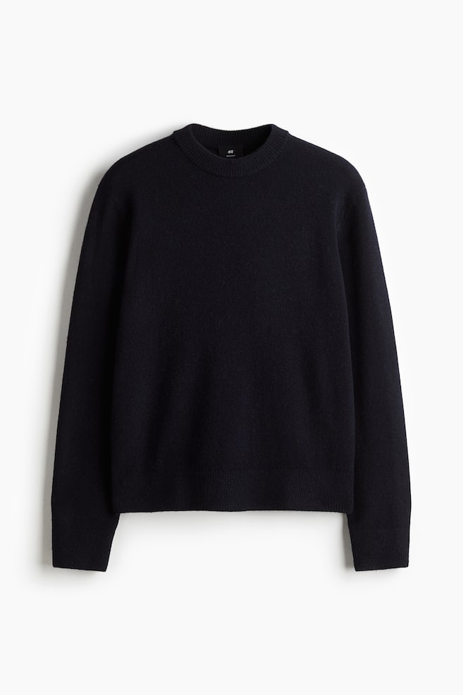 En sort finstrikket sweater med rund hals vender fremad. Den har lange ærmer med ribbede manchetter og en ribbet kant. - 1