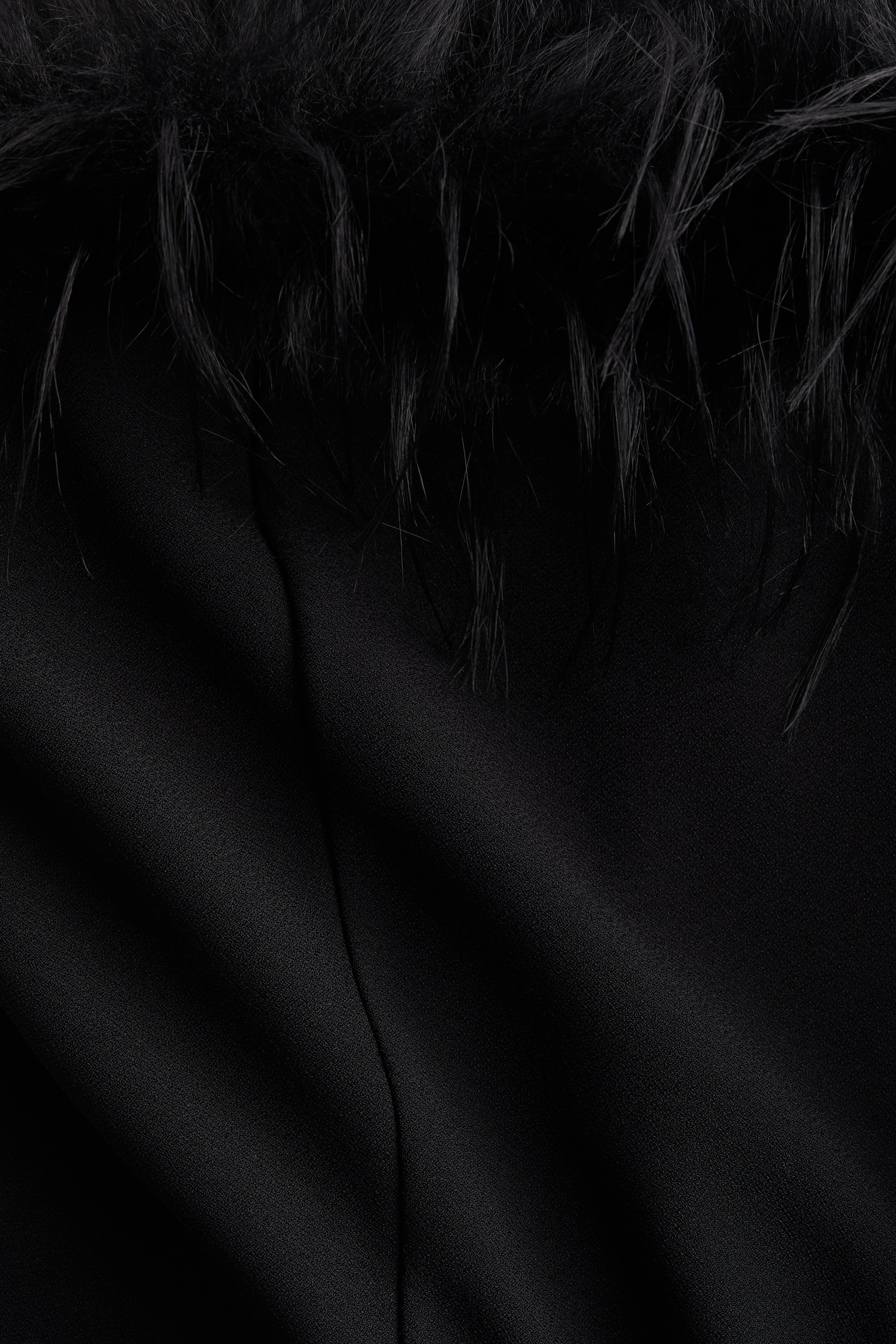 Agrandir l'image: Un vêtement noir présente un tissu noir texturé avec des plis subtils, et des plumes noires forment une bordure le long du bord supérieur.