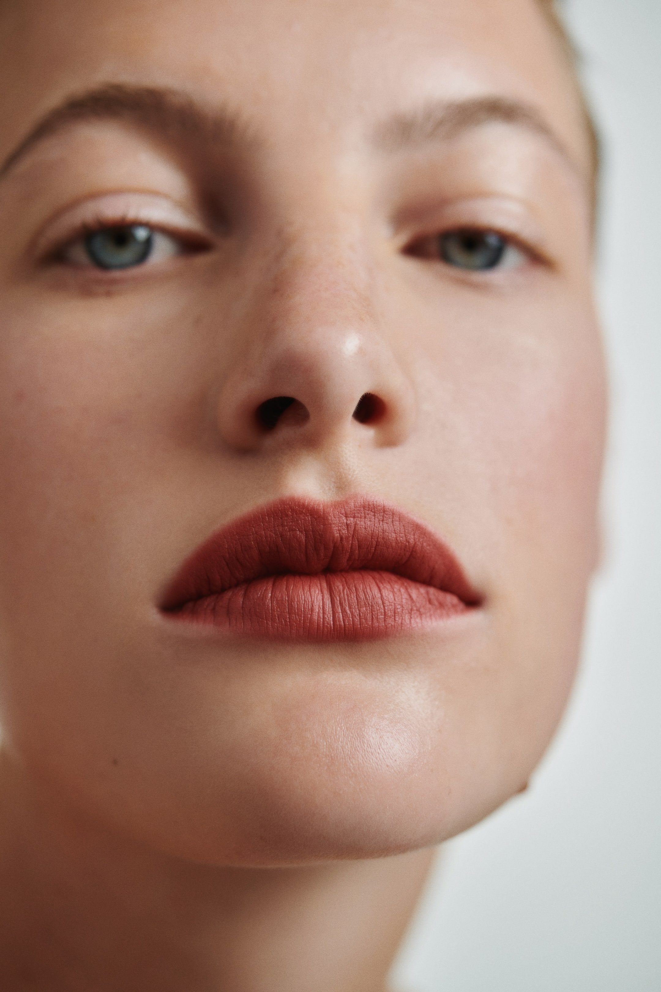 View larger image: A muted brick-red lipstick is applied to the lips, showcasing a matte finish with a smooth application.