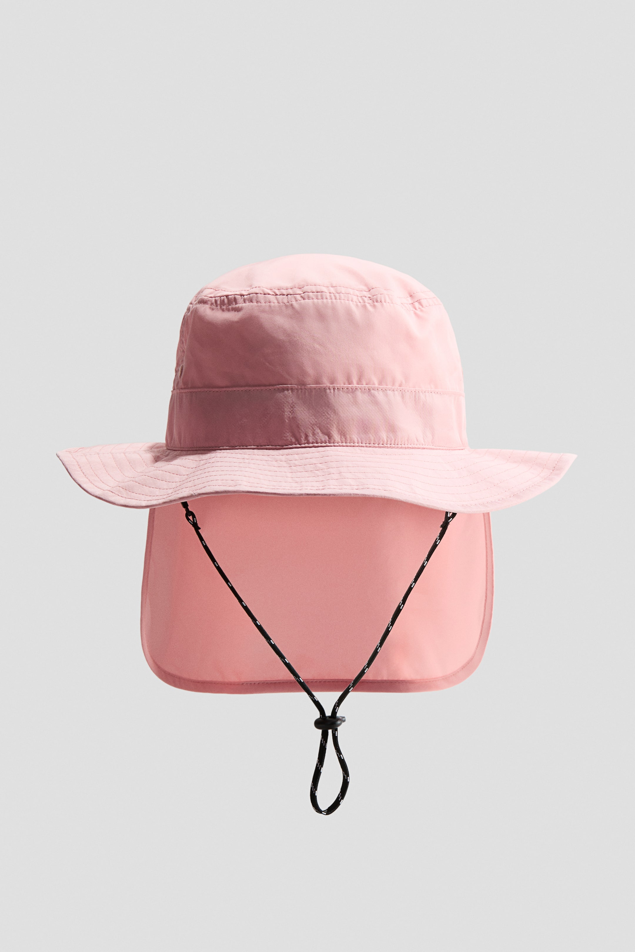 Ampliar la imagen: Un sombrero de sol rosa se presenta de frente, con un ala ancha e inclinada y una solapa para el cuello plegable a juego. Un cordón ajustable en blanco y negro con un tope de cordón se extiende desde debajo del ala.