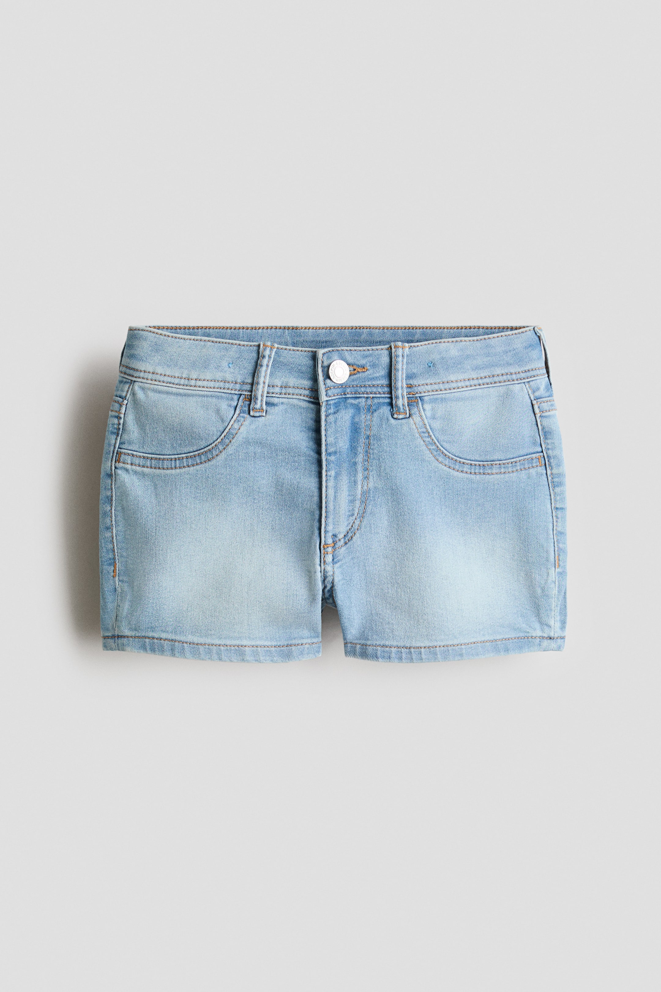 Grösseres Bild ansehen: Hellblaue Jeansshorts werden aus einer Frontalperspektive präsentiert und verfügen über einen Bund mit fünf Gürtelschlaufen. Ein weißer Metallknopfverschluss ist in der Mitte sichtbar, darunter verläuft eine Reißverschlussnaht. Zwei geschwungene Vordertaschen sind mit Nähten umrandet, und die Beinabschlüsse sind mit Nähten versehen.