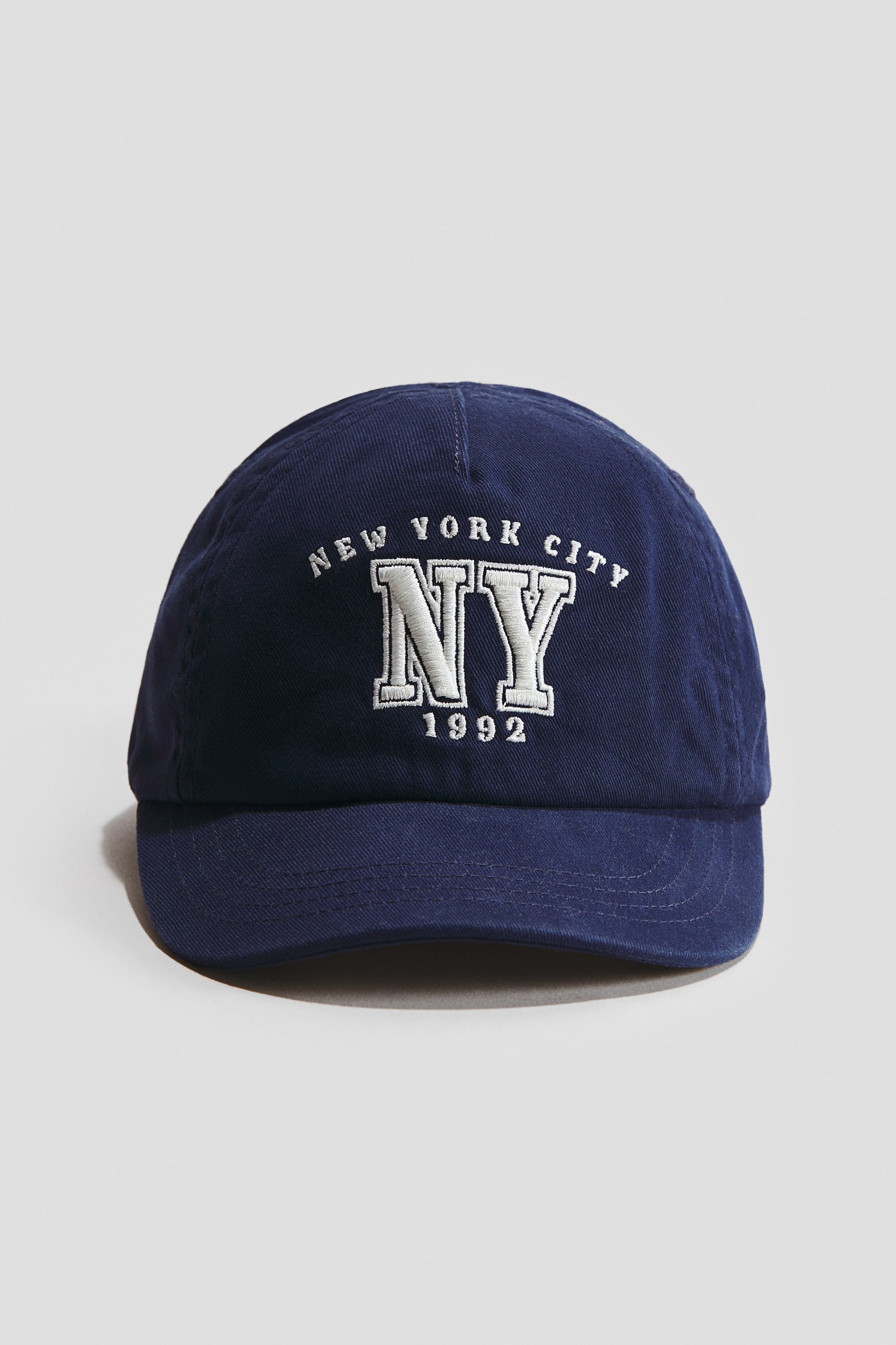 View larger image: A navy blue cap is facing front, showcasing a cotton weave. The front displays white embroidered text, with 'NEW YORK CITY' arcing above large 'NY' letters and '1992' below.