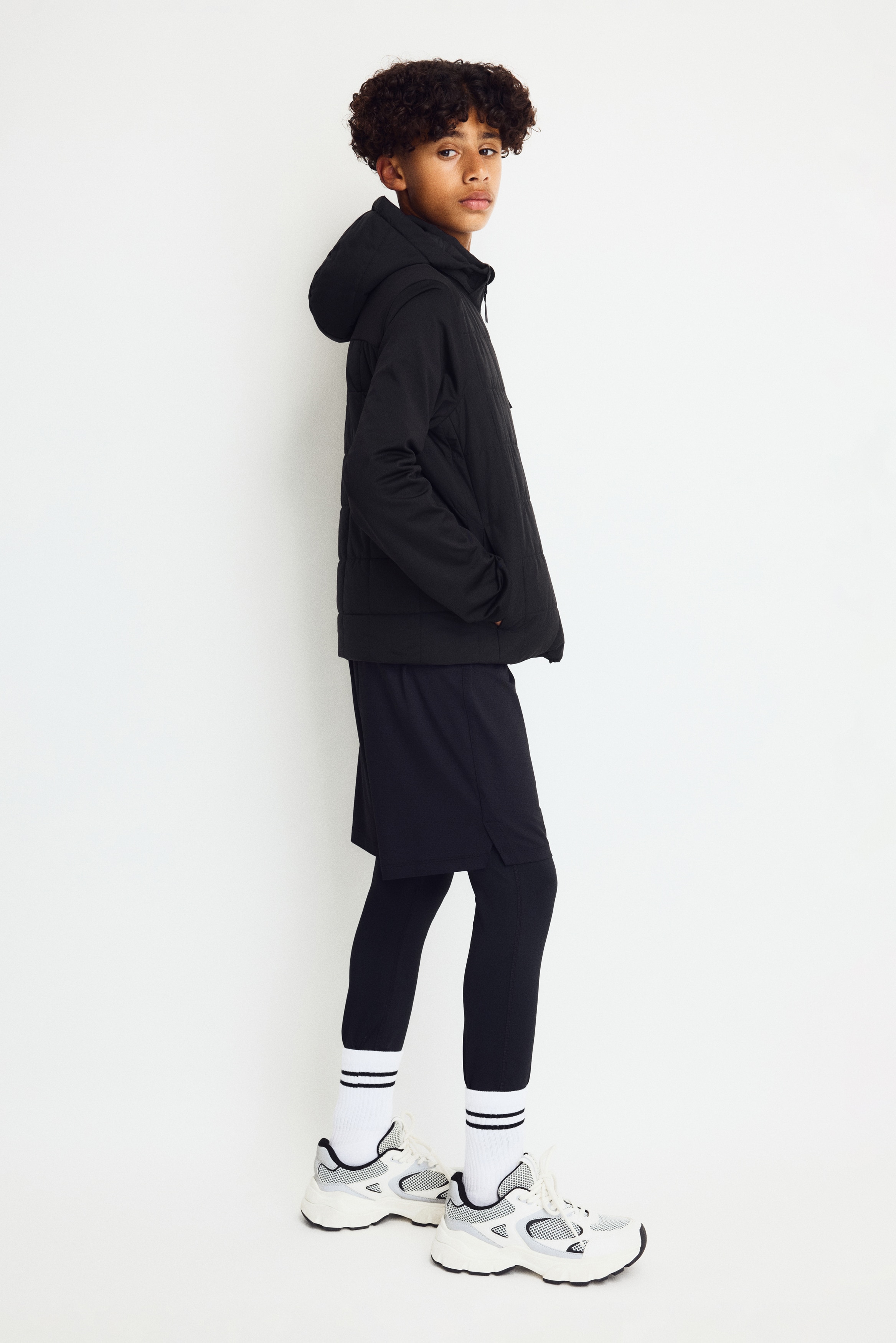 The image showcases a black jacket, front-facing, with a square-quilted front body and hood, complemented by solid black sleeves. It features a full-length central zipper, a vertical zippered pocket on the left chest, and the text "THERMOMOVE" positioned vertically on the lower right sleeve.