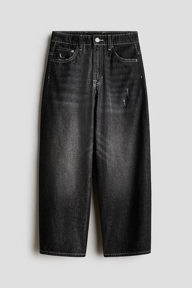 Baggy 5-pocket jeans in washed black cotton denim are hanging in a front view, displaying a wide-leg silhouette with light contrast stitching. The jeans are featuring a faded wash down the thighs, a classic button-and-zip fly closure, and subtle distressed details on the coin pocket and left thigh. - 1
