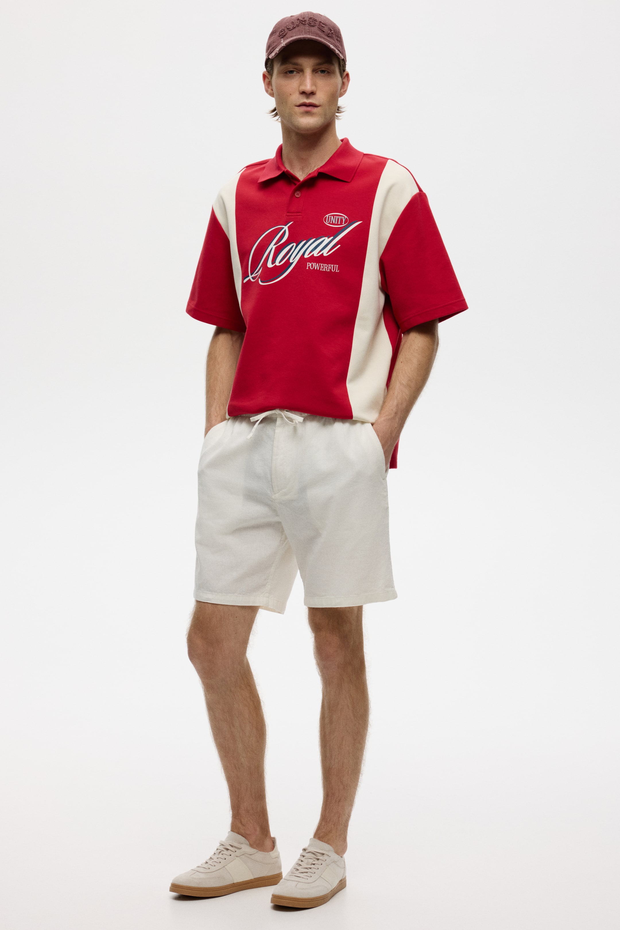View larger image: The polo shirt features a red and cream colour-block design, with red on the chest and sleeves and cream panels running down the sides. It displays a two-button placket and a prominent white "Royal" graphic on the chest, accompanied by smaller "Unity" and "Powerful" text.