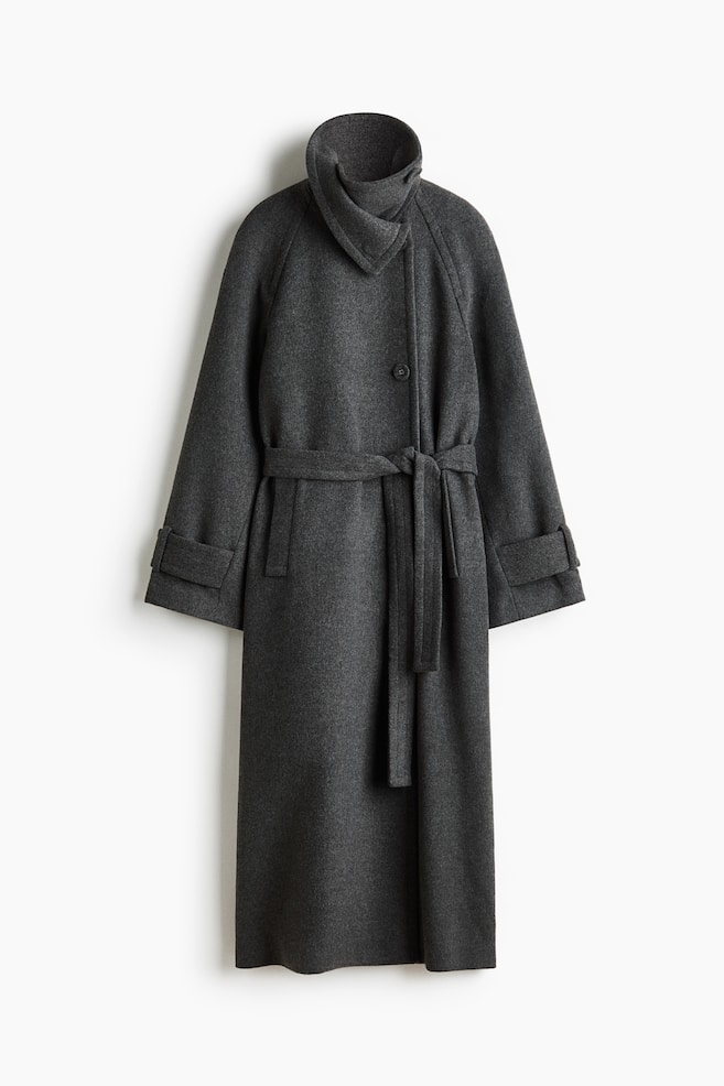 A dark grey wool-blend wrap coat is shown from the front, featuring a high, structured funnel collar with an asymmetrical wrap design and a single-button closure. The coat is styled with a matching self-tie belt at the waist, raglan sleeves with wide tabbed cuffs, and discreet side pockets. - 1
