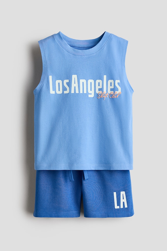 A light blue sleeveless tank top and dark blue shorts set is displaying from the front. The tank top is featuring a round ribbed neckline and "Los Angeles Skate Club" printed in white and orange on its front, while the shorts are including a drawstring waist and "LA" printed in white on the left leg. - 1