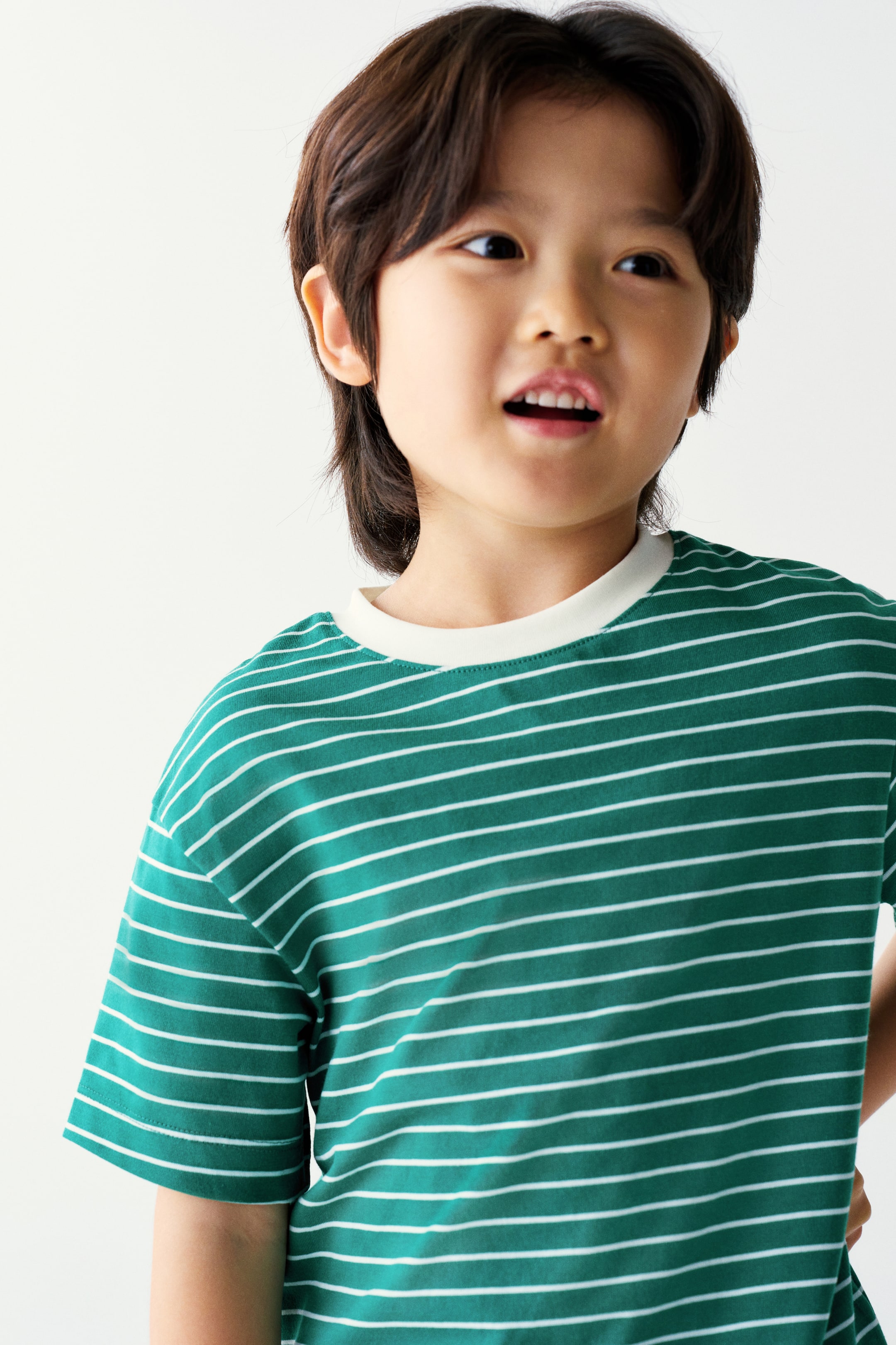 View larger image: The model is wearing a green short-sleeved T-shirt with thin horizontal white stripes and a contrasting white crew neck.
