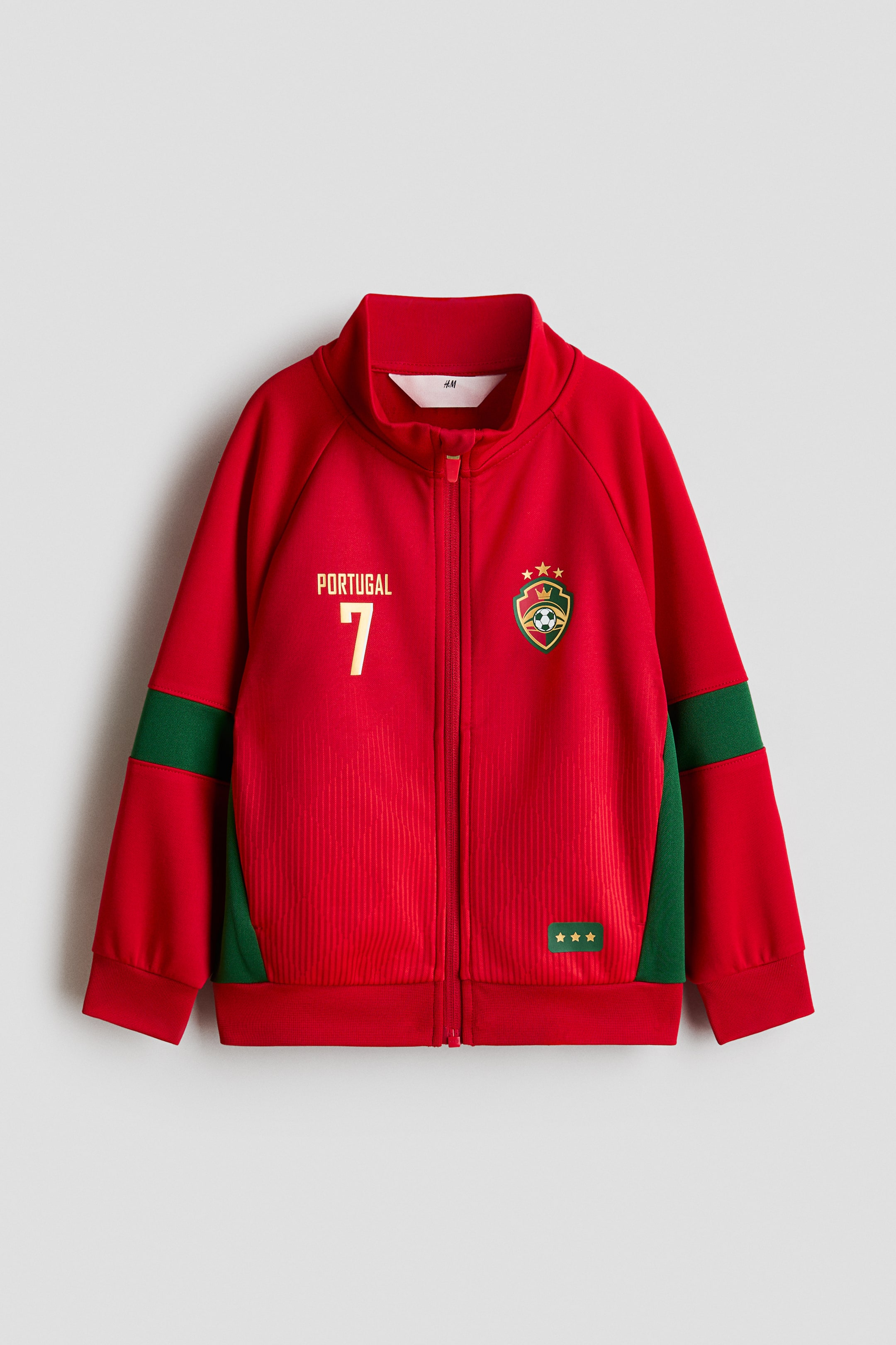 View larger image: A red track jacket with a subtle sheen is shown FRONT, featuring a stand-up collar, a full zip fastening with a chin guard, and a subtle vertical ribbed texture on the main body. "PORTUGAL" and the number "7" appear in gold on the left chest, an embroidered crest is visible on the right, and green panels run along the long raglan sleeves, which are finished with ribbed cuffs and hem.