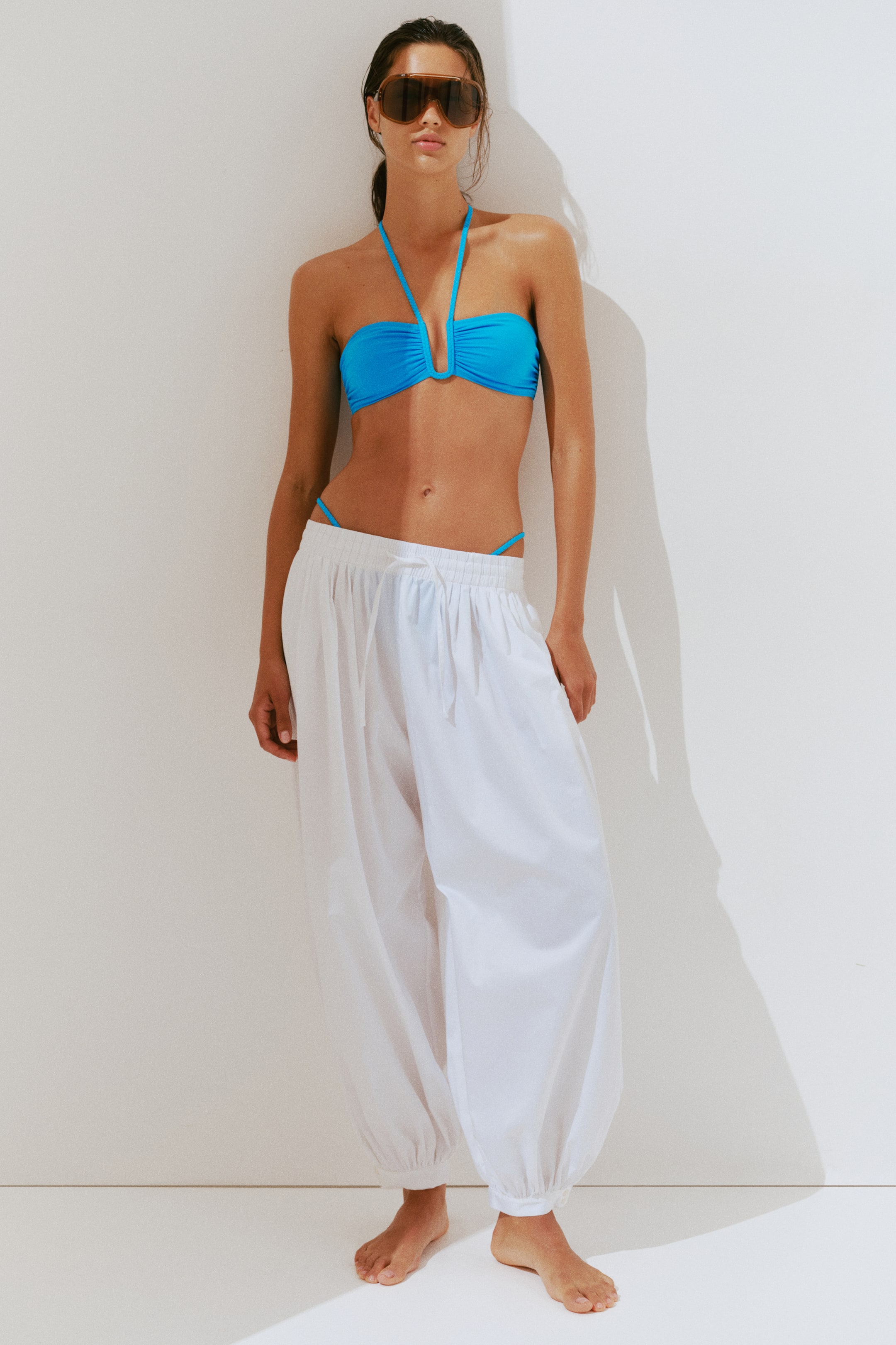 View larger image: The model is wearing a blue bandeau bikini top with a U-shaped wire detail at the center of the bust and braided halter neck ties.