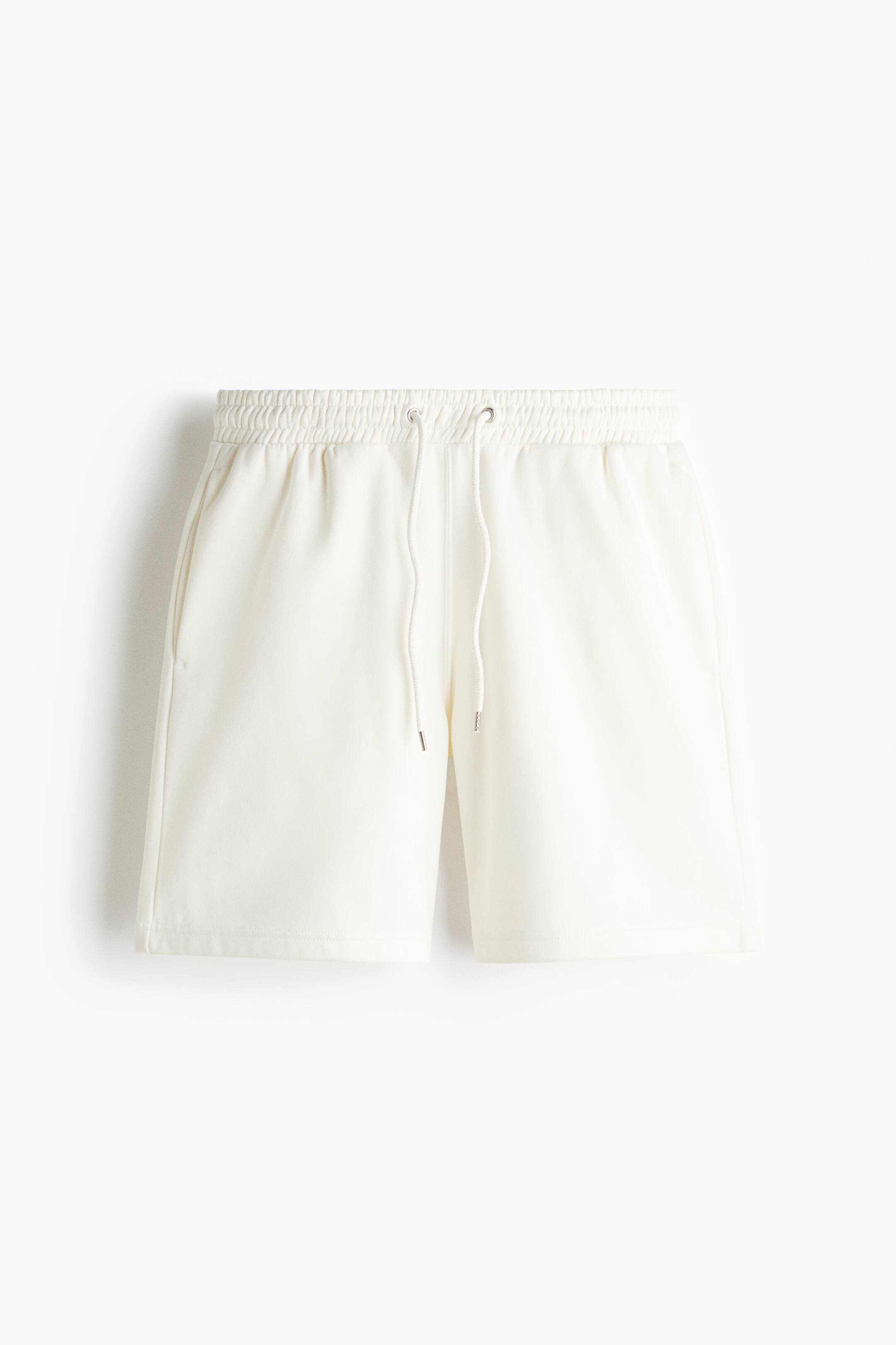 View larger image: Cream-coloured jersey shorts are shown from the front, featuring an elasticated, gathered waistband with an adjustable drawstring. The shorts are displaying a regular fit with side slip pockets and a clean, straight-cut hem.