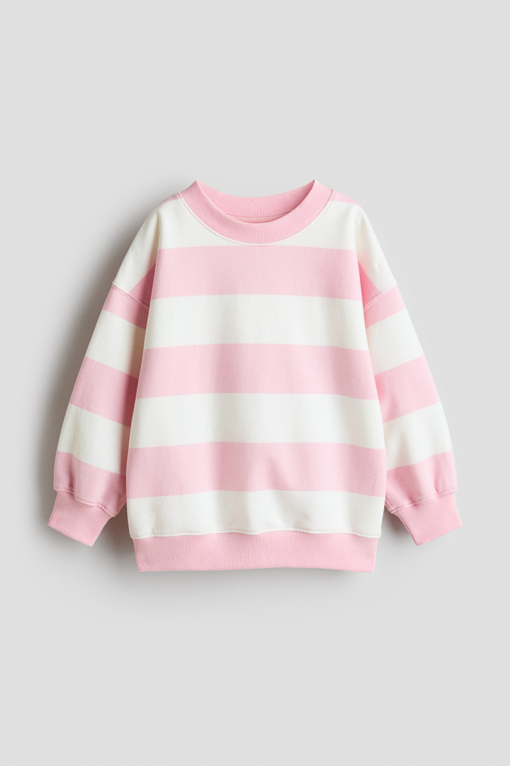 Visa större bild: En oversized sweatshirt visar sin FRAMSIDA, med horisontella rosa och vita ränder. Den har en rund halsringning med ribbkant, nedhasade axlar, långa ärmar med ribbade muddar och en ribbad fåll.