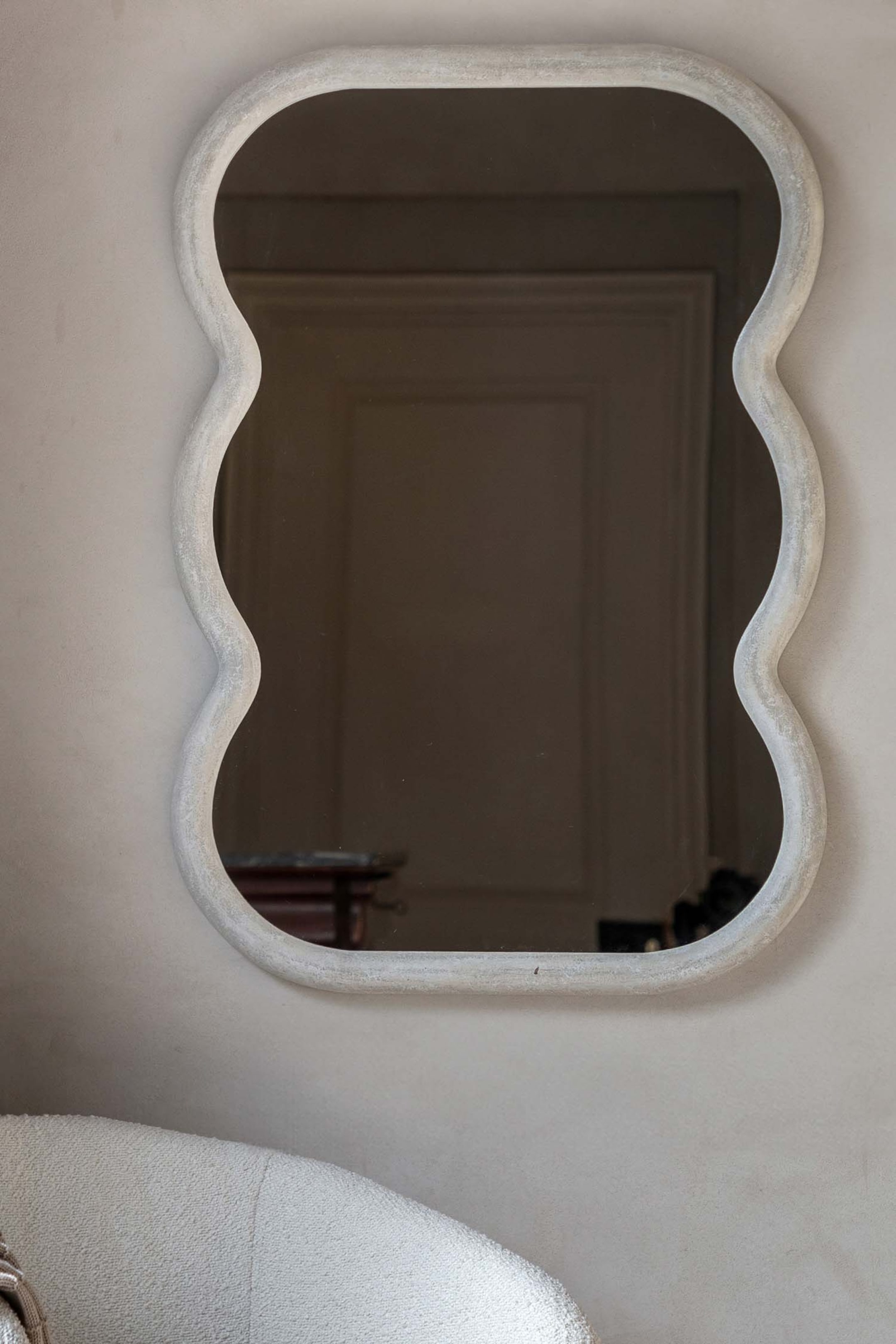 View larger image: A mirror featuring an organic, undulating shape with a textured, light-coloured frame. It is mounted flat against a surface.