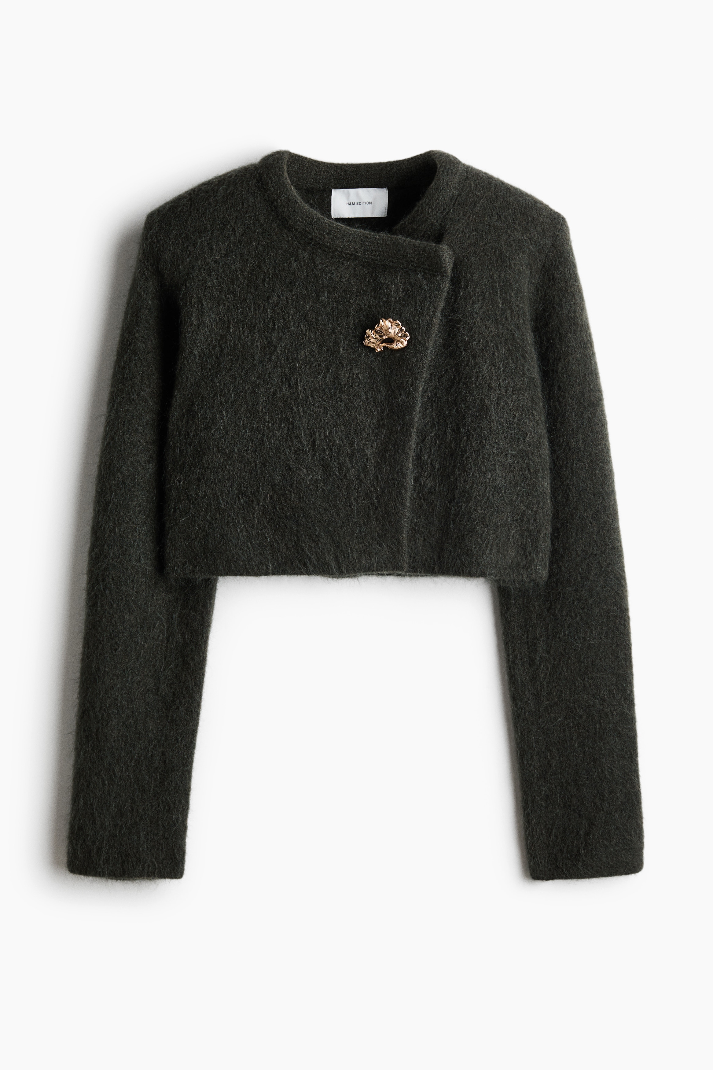 La modelo lleva un cÃ¡rdigan recortado de mezcla de mohair en gris oscuro con los brazos cruzados. El cÃ¡rdigan presenta una textura de punto afelpado, hombreras estructuradas, un escote redondo y un cierre frontal descentrado con un botÃ³n decorativo dorado.