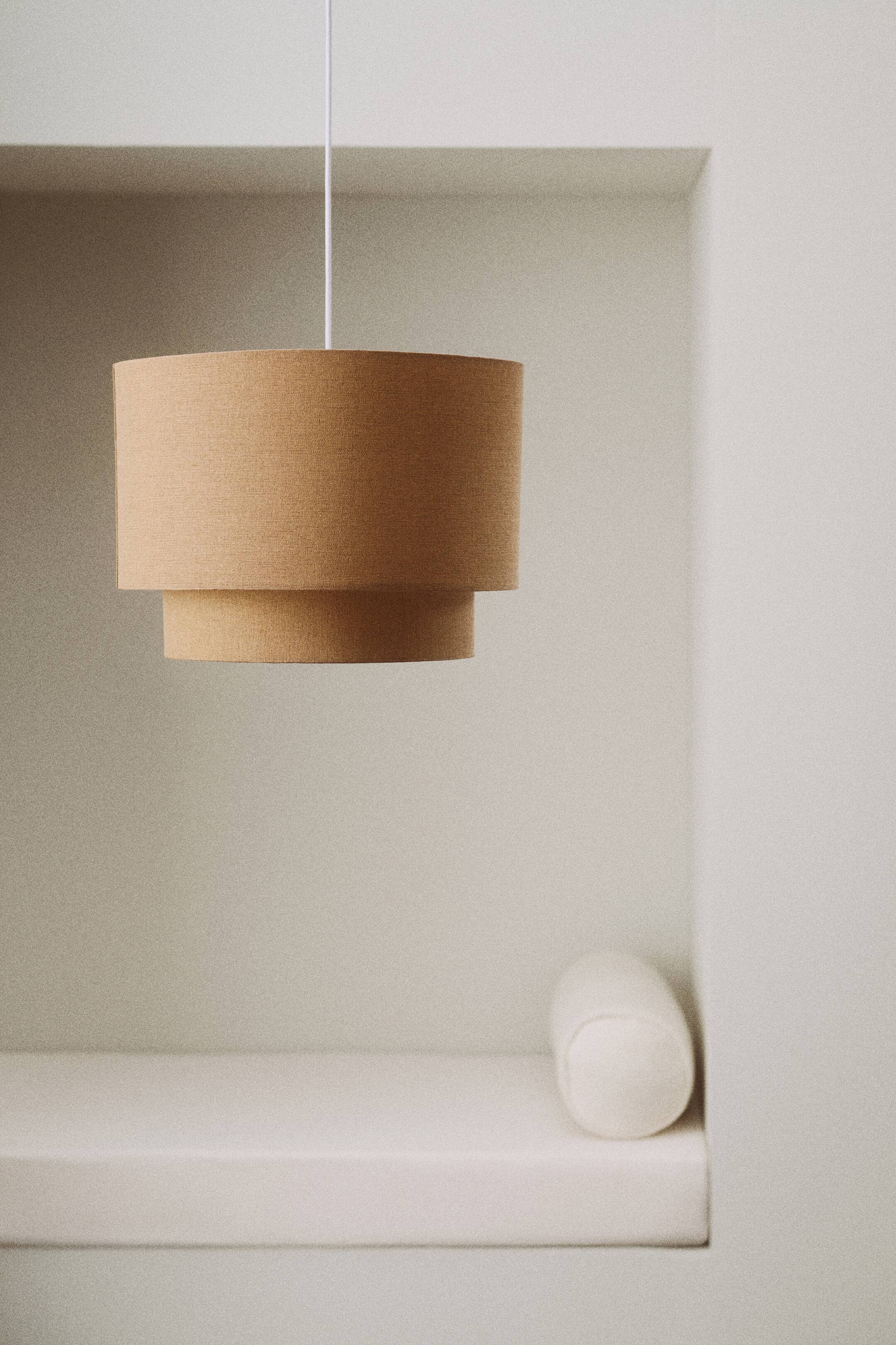 View larger image: A pendant light featuring a layered cylindrical fabric shade in a light brown hue, suspended from a white cord, with its front view showcasing its tiered design.