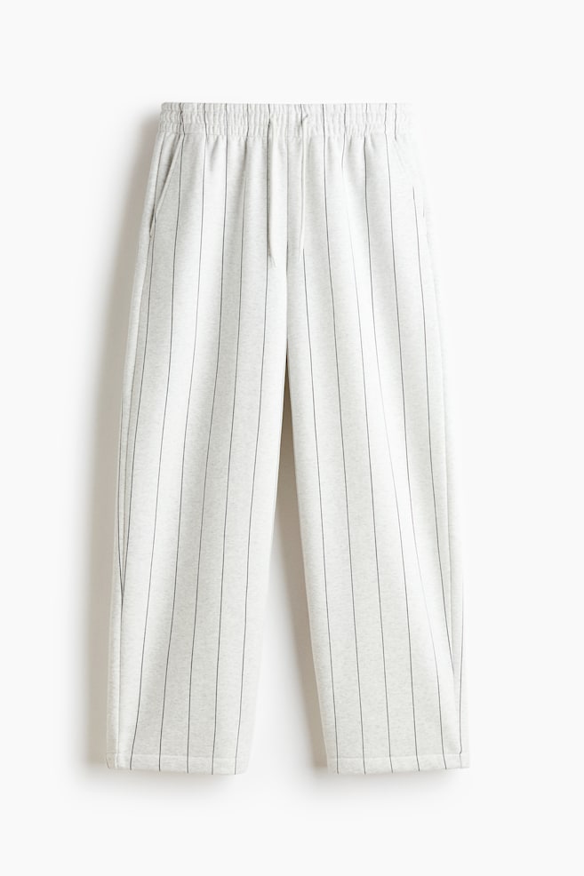 These light grey melange track pants are hanging in a front-facing view, showcasing a relaxed barrel-leg silhouette with thin, black vertical pinstripes. The trousers feature an elasticated waistband with a drawstring and diagonal side pockets. - 1