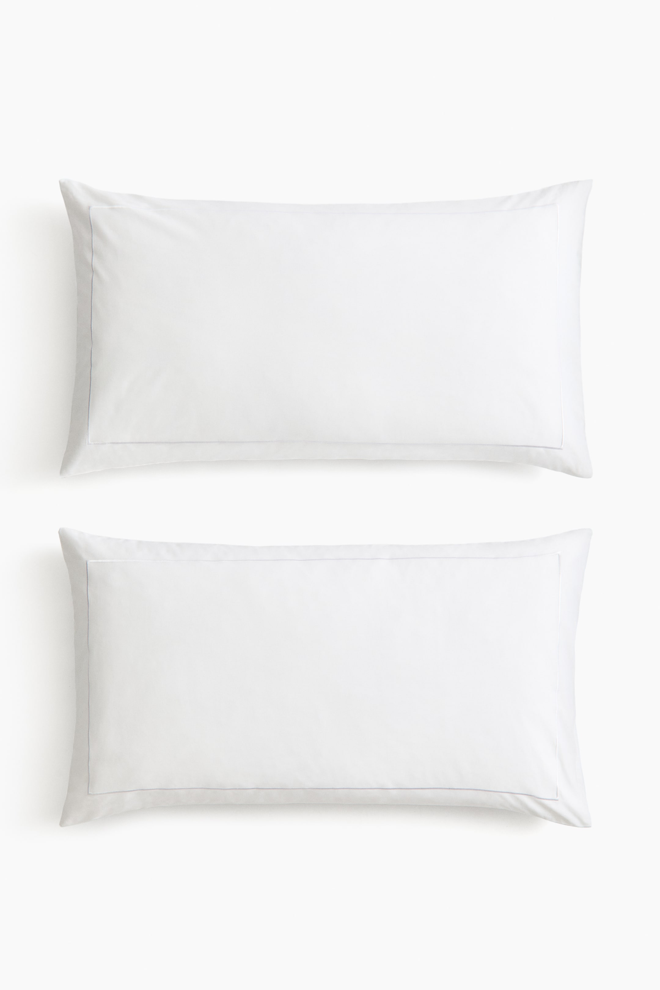 View larger image: Two white pillowcases are lying flat, each featuring a light grey stitched border outlining the perimeter.