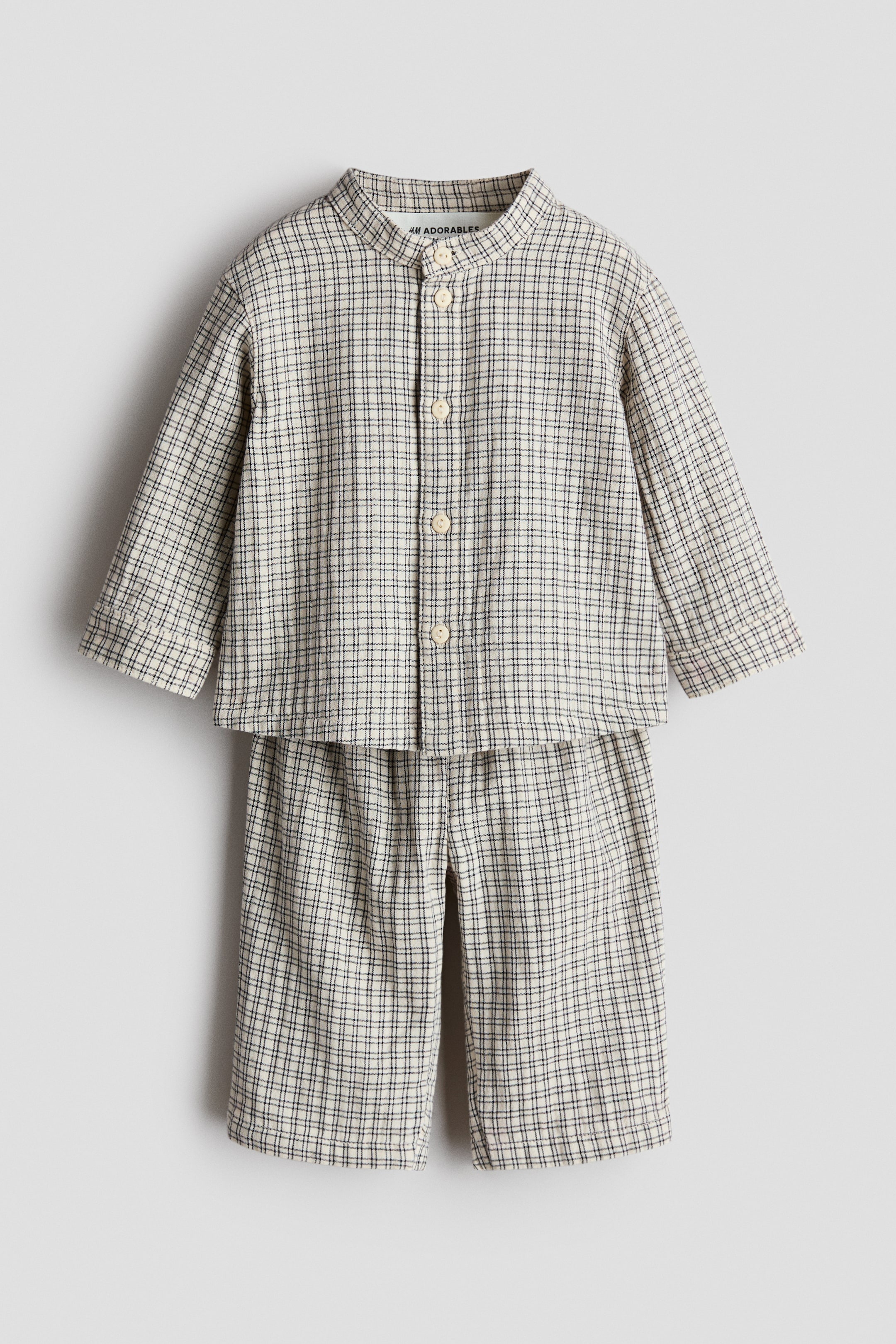 View larger image: A two-piece children's clothing set, showcasing a beige and black grid pattern, is displayed from the front. The long-sleeved shirt features a band collar and a button-front placket, while the matching trousers exhibit a relaxed fit with an elasticated waistband.
