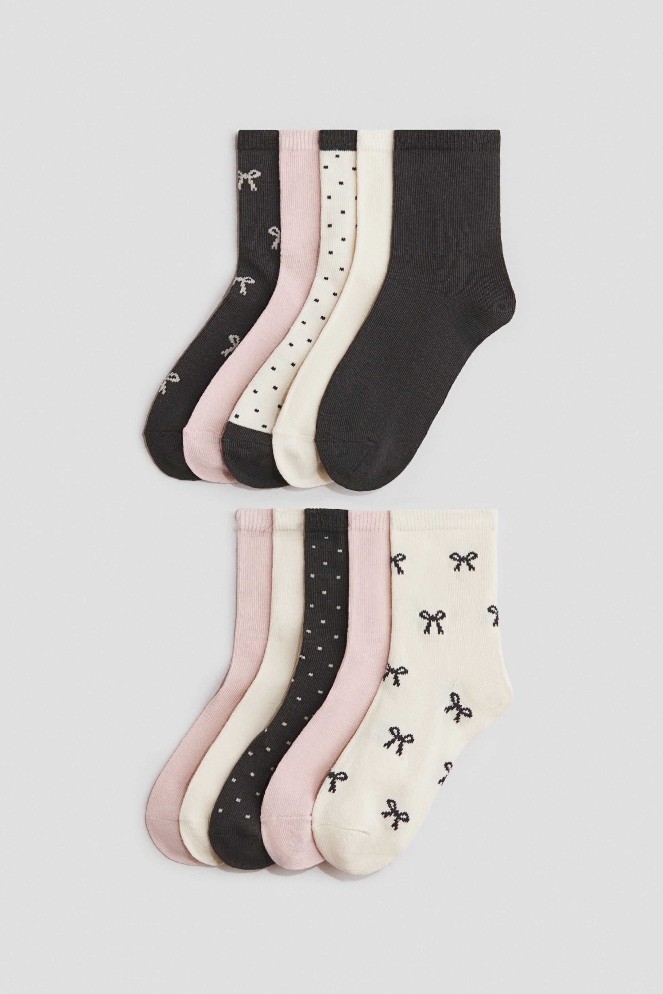 View larger image: Ten fine-knit socks are displayed in two fanned-out groups, each showcasing five distinct designs: solid dark grey, solid light pink, cream with black polka dots, cream with black bow patterns, and solid cream, all with elasticated tops.